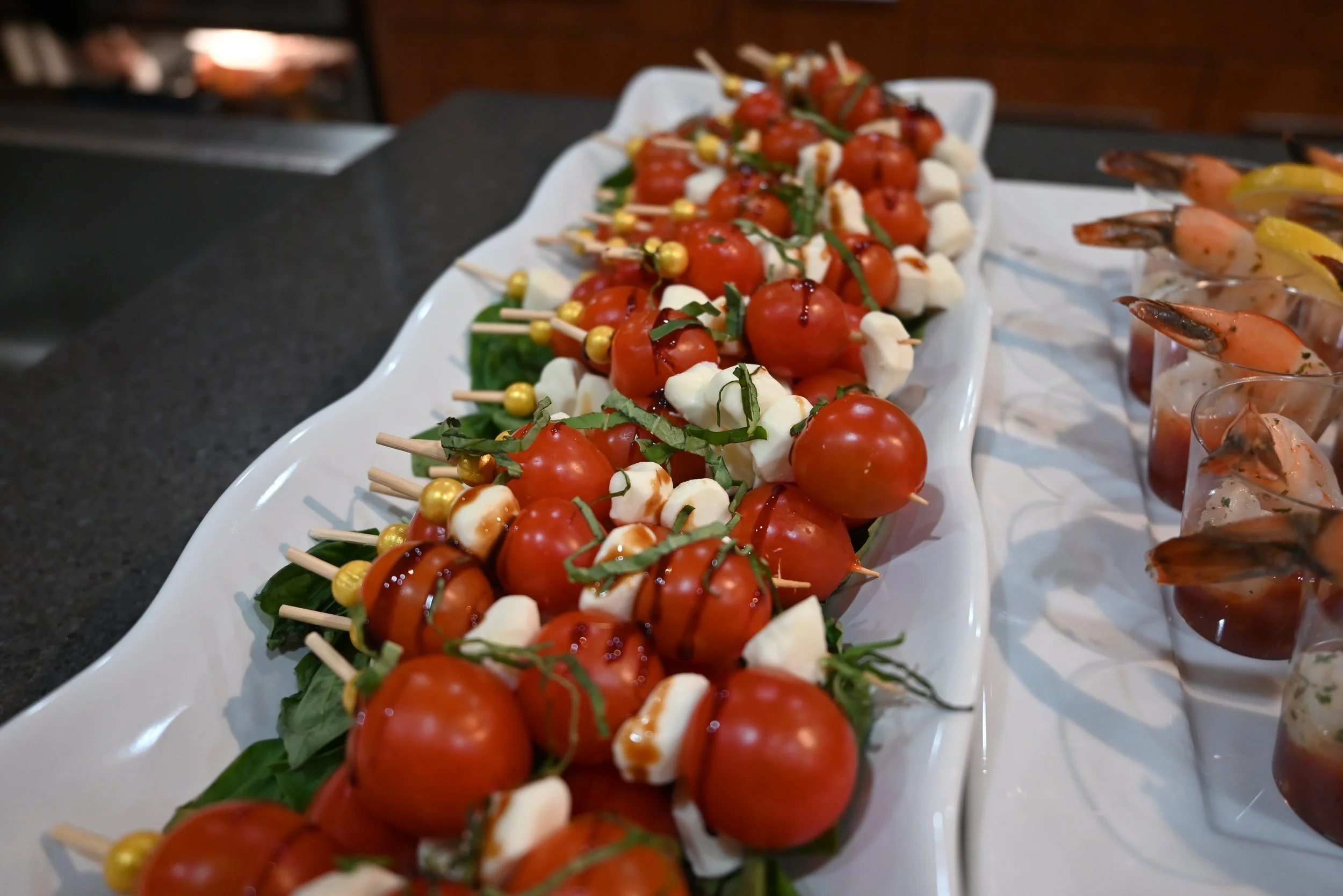Skewers with cherry tomatoes, mozzarella balls, basil, and balsamic glaze, arranged on a white platter.