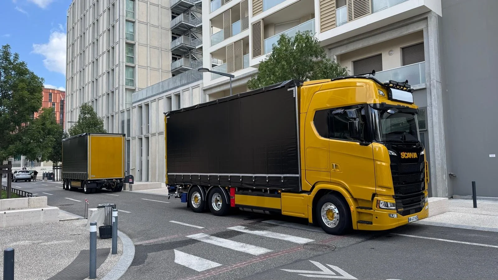 Un camion de livraison jaune et noir stationné dans une zone urbaine, avec des bâtiments modernes en arrière-plan.