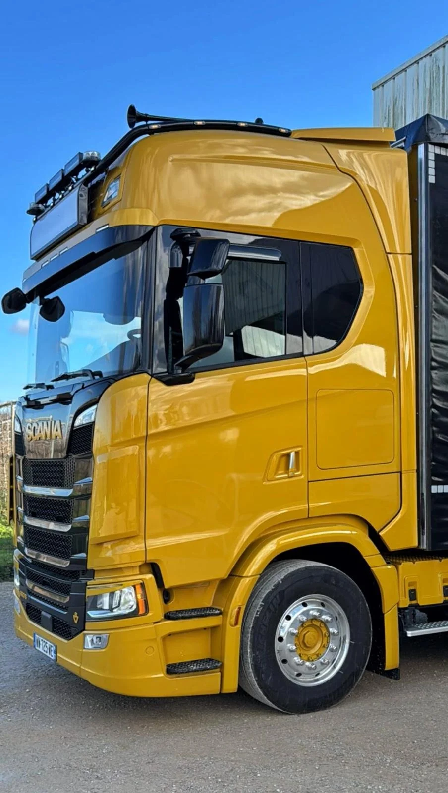 Camion de couleur jaune garé sur le côté d'une route sous un ciel bleu clair.