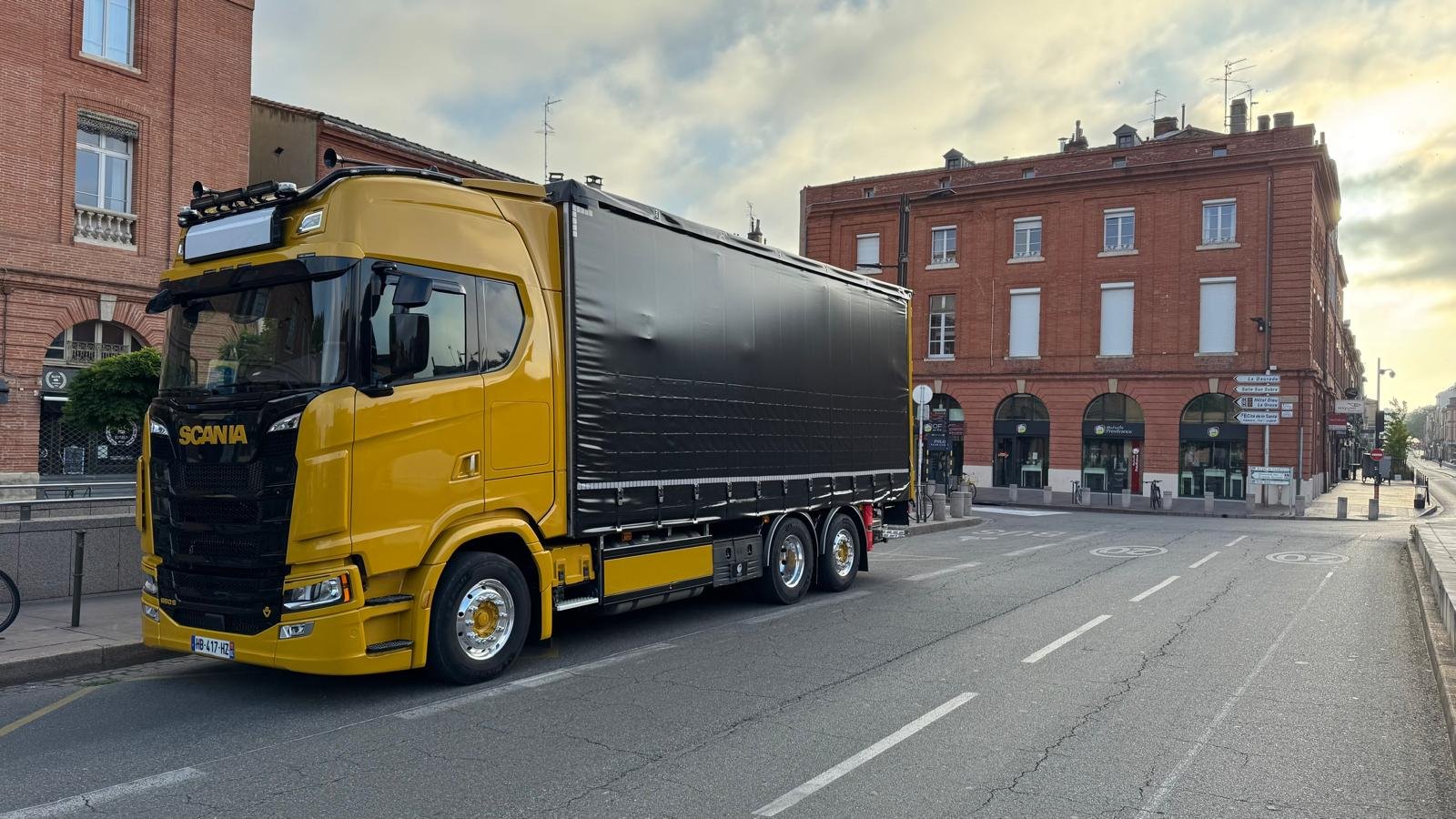 Camion de couleur jaune avec un conteneur noir stationné dans une rue urbaine