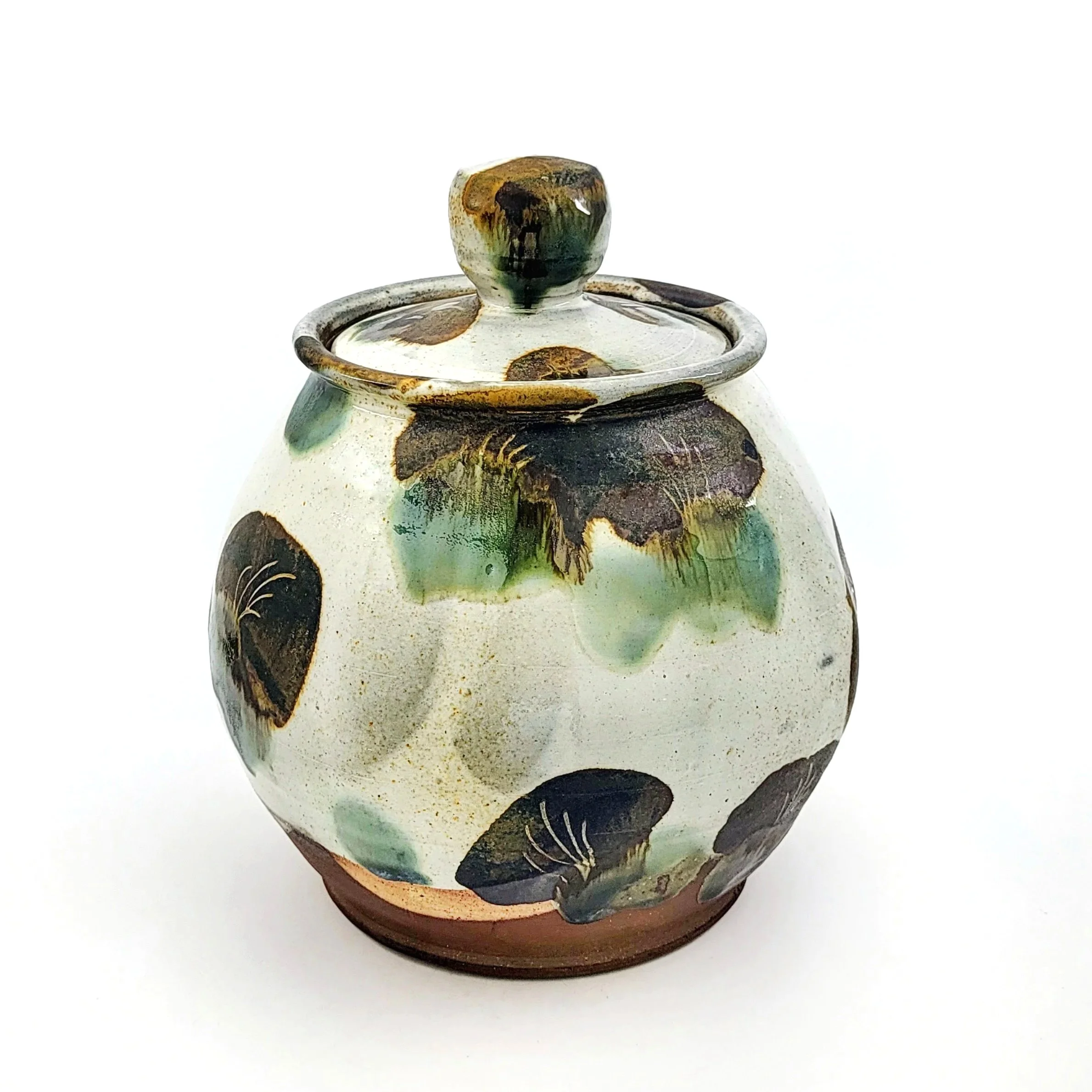Decorative ceramic jar with a lid, featuring painted dark brown and green leaves on a cream background, and a brown bottom edge.