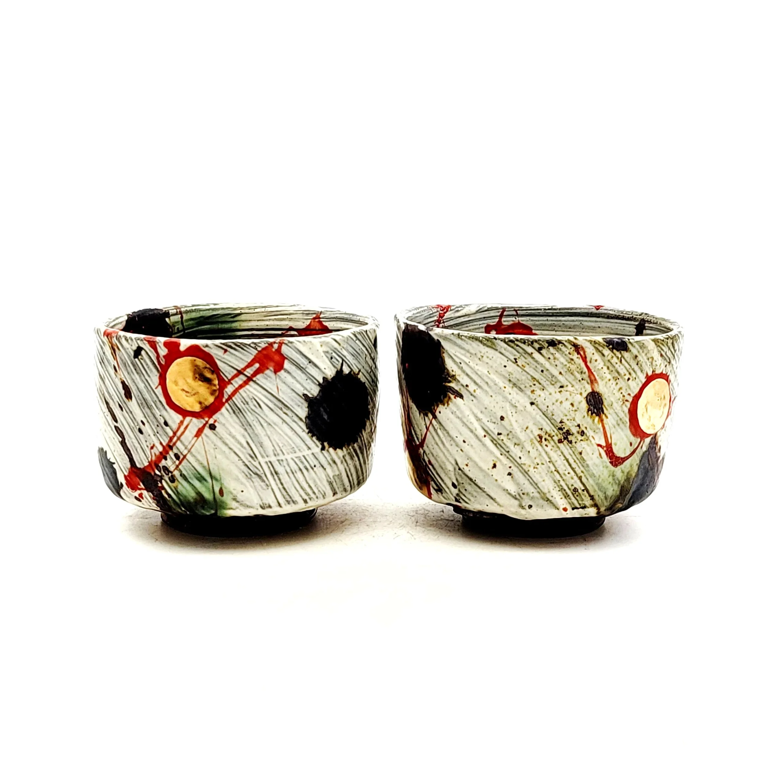 Two ceramic bowls with abstract black, red, yellow, and green splashes and streaks on a white background