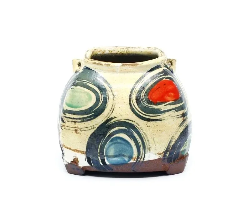 Ancient ceramic vessel with colorful concentric circle patterns and a small red and green accent on a white background.