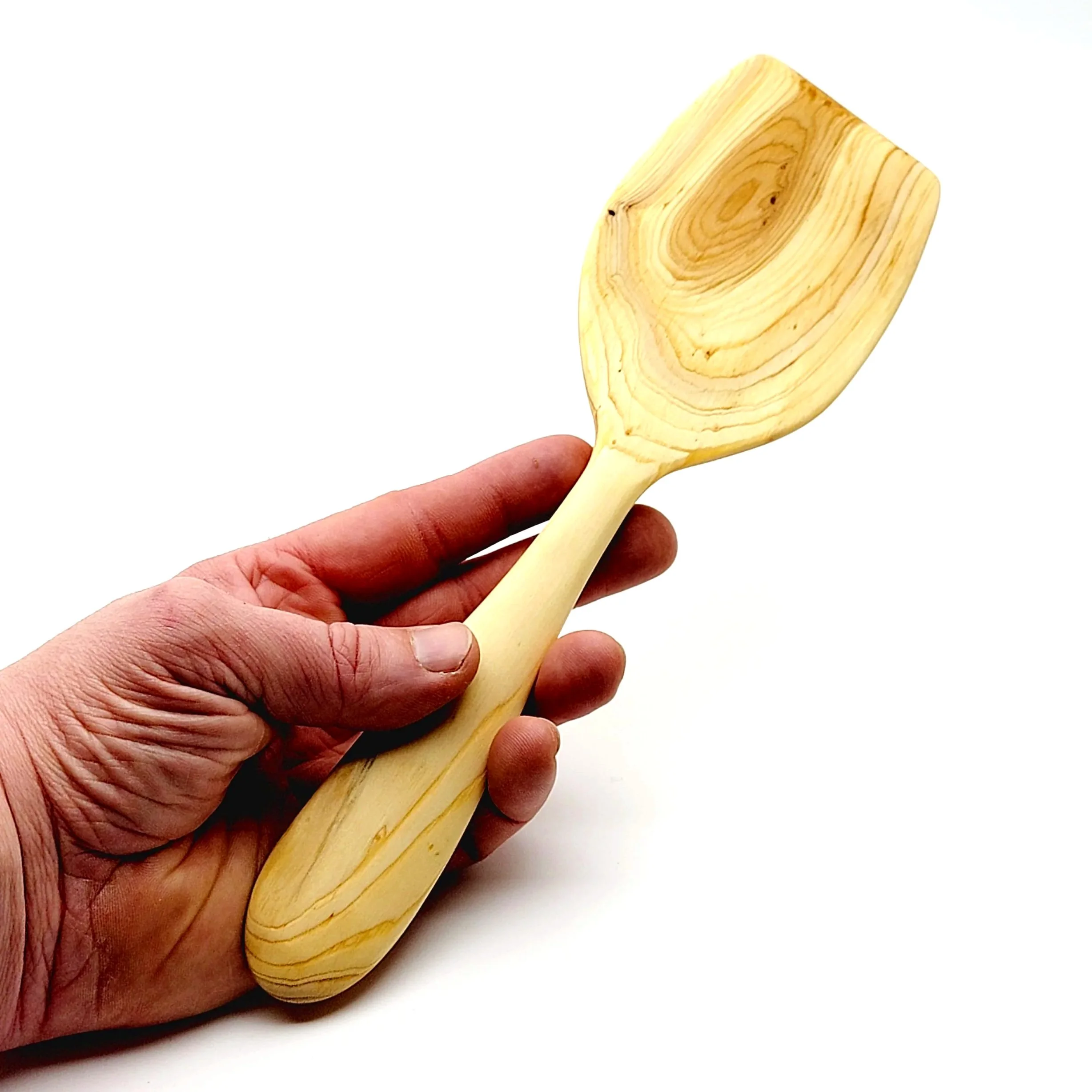 A hand holding a wooden spatula with a flat, wide blade and handle, made of light-colored wood.