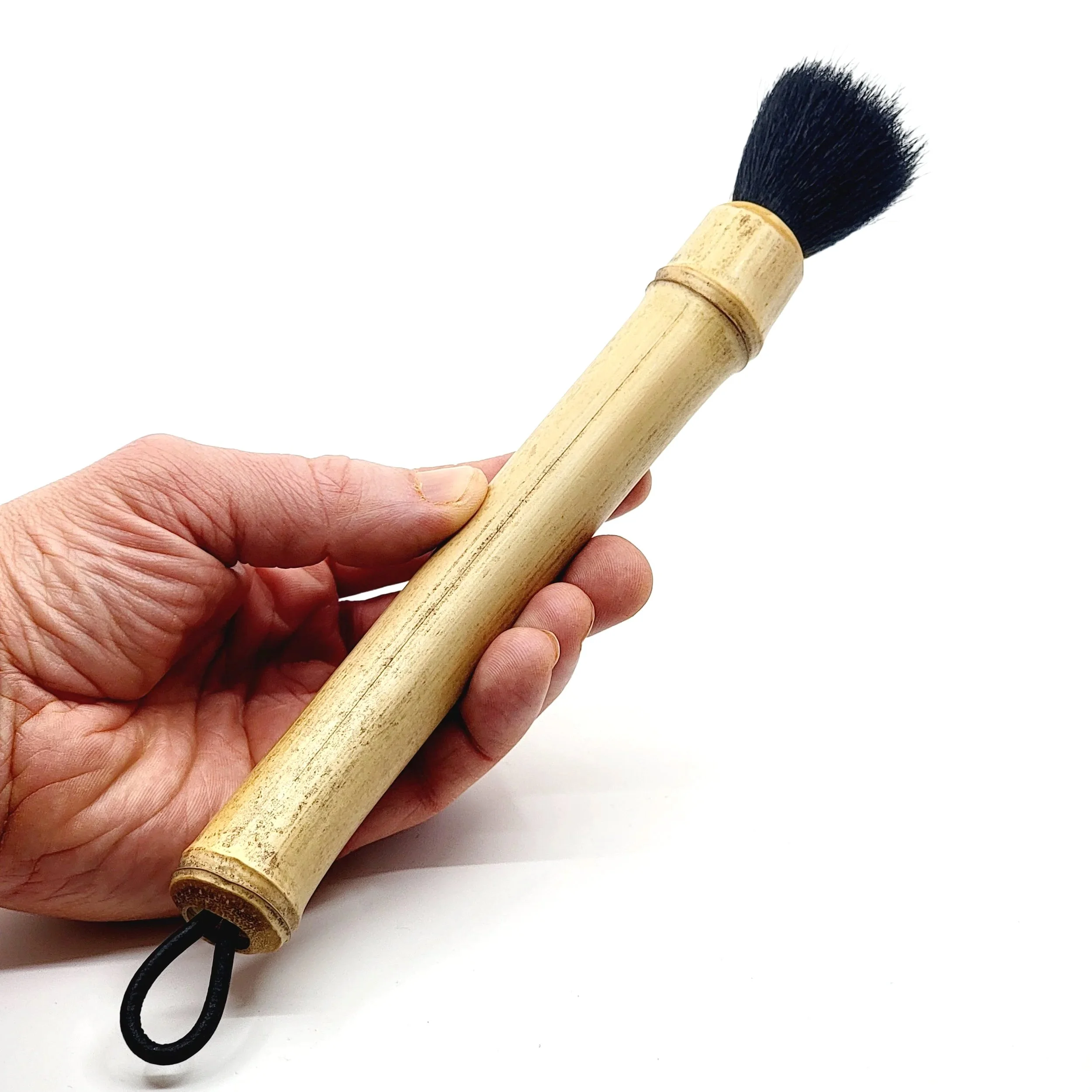 Hand holding a bamboo whisk with black handle and handle loop on a white background.