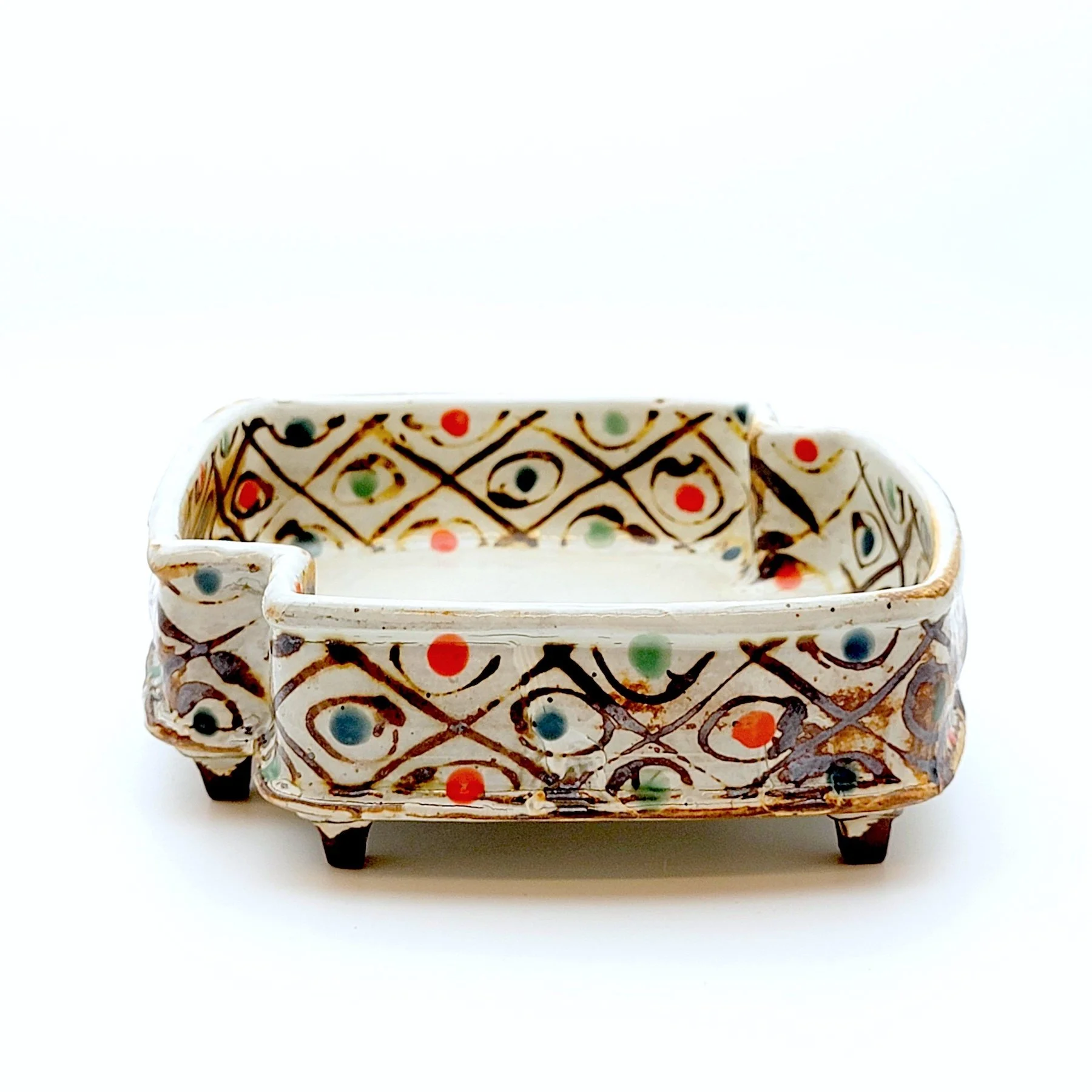 Small rectangular ceramic dish with colorful geometric and dot patterns, raised on four legs.