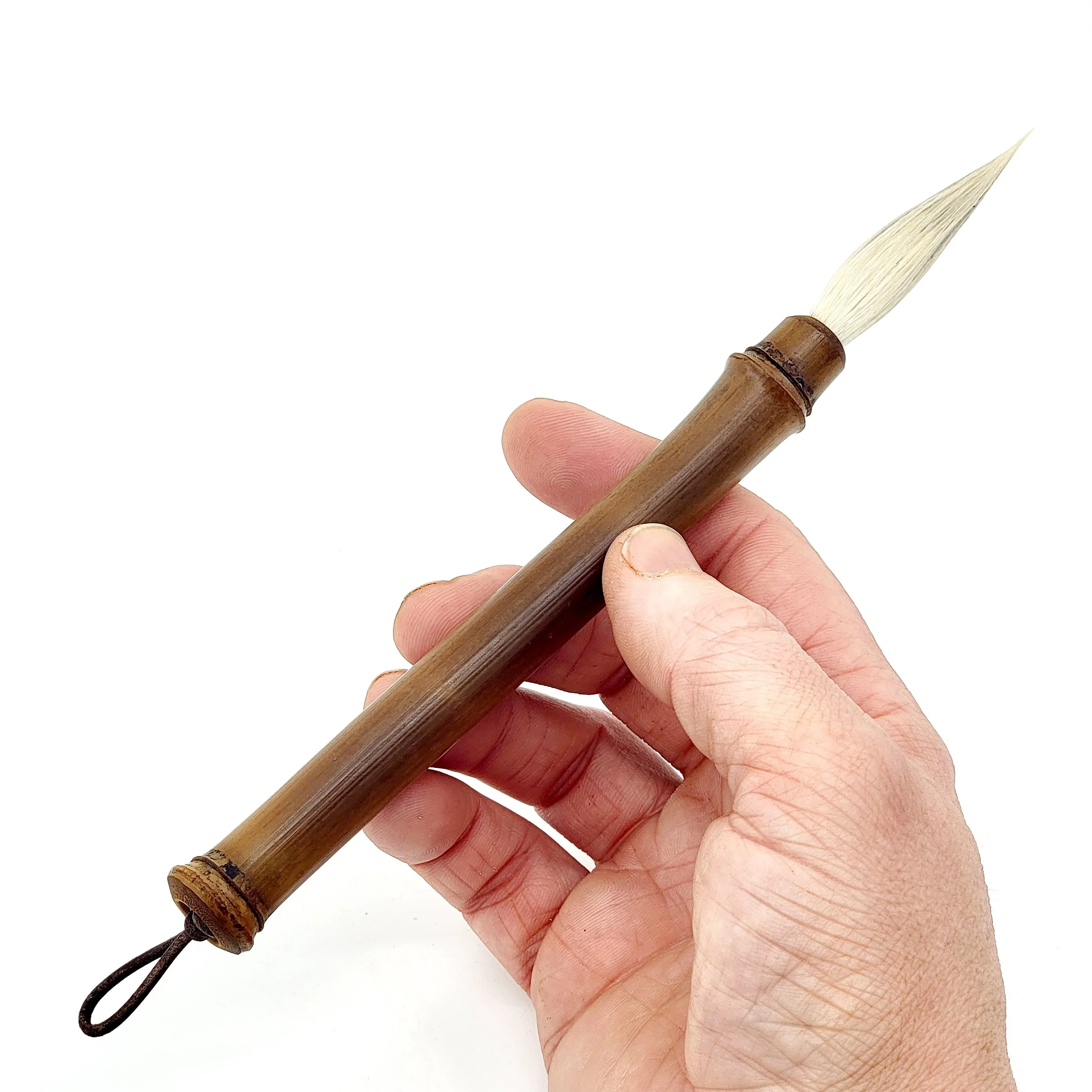 A hand holding a traditional Asian calligraphy brush with a wooden handle and white bristles against a white background.