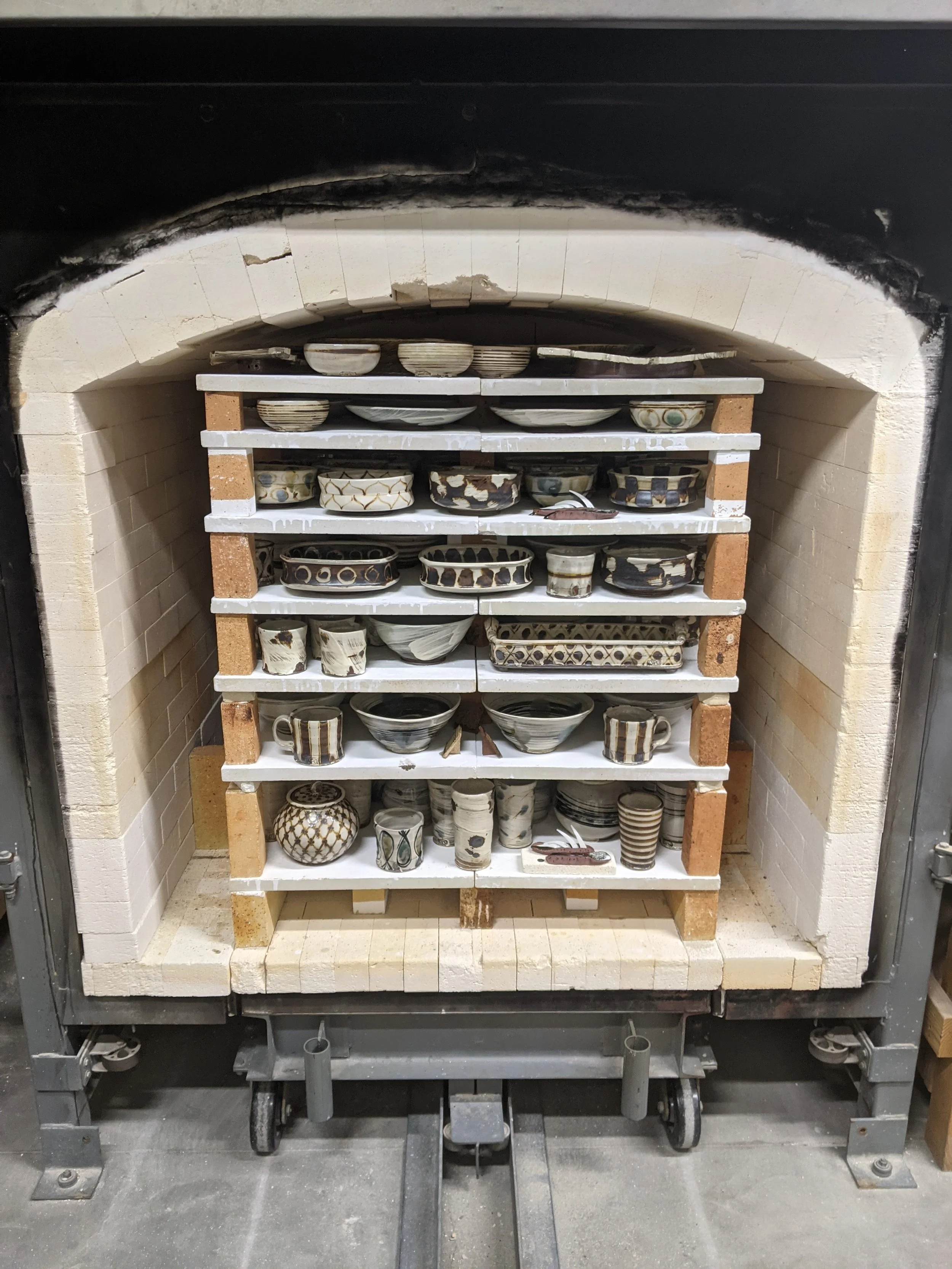 Collection of ceramic bowls and cups on shelves inside a kiln.
