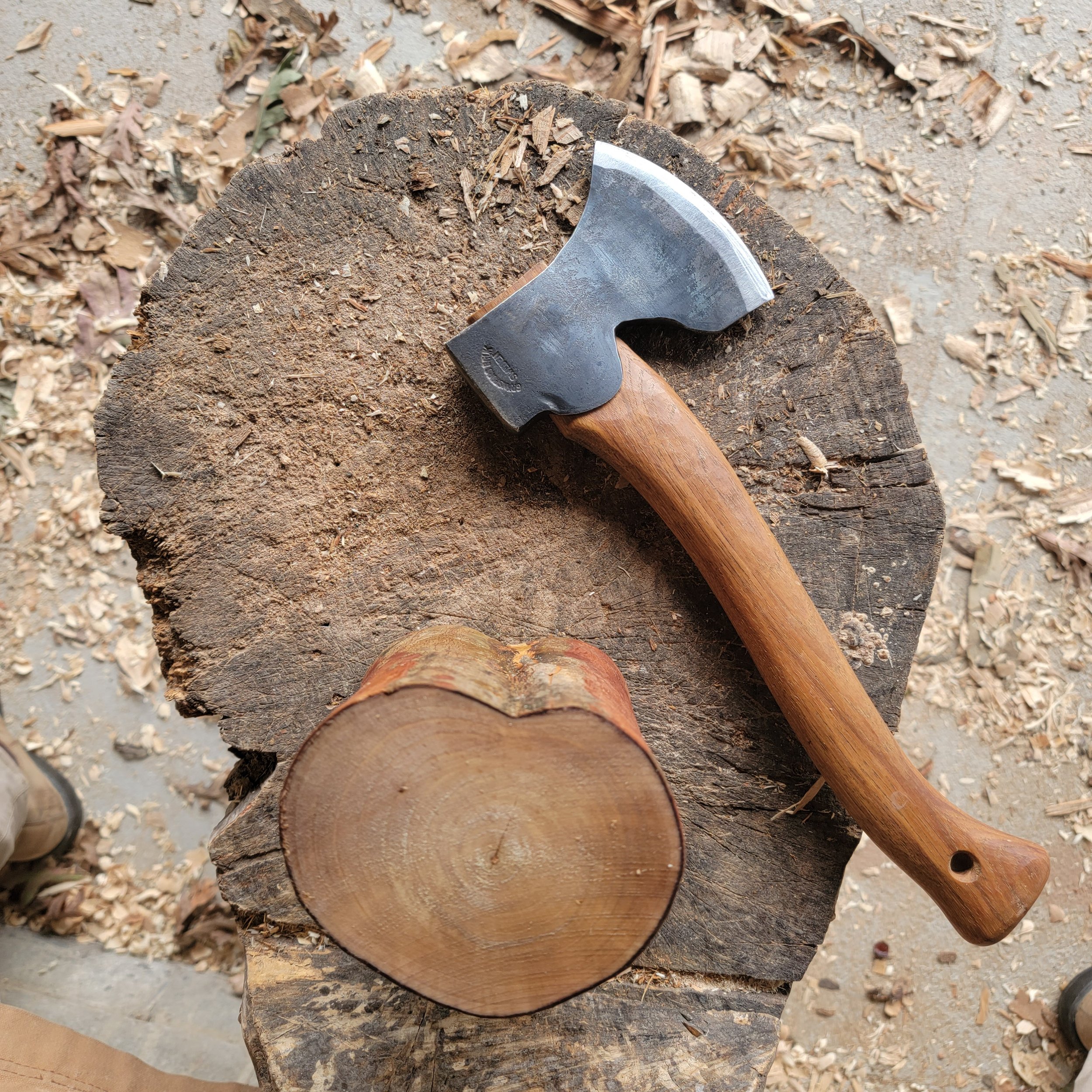 An axe resting on a tree stump with sawdust and wood shavings scattered around.