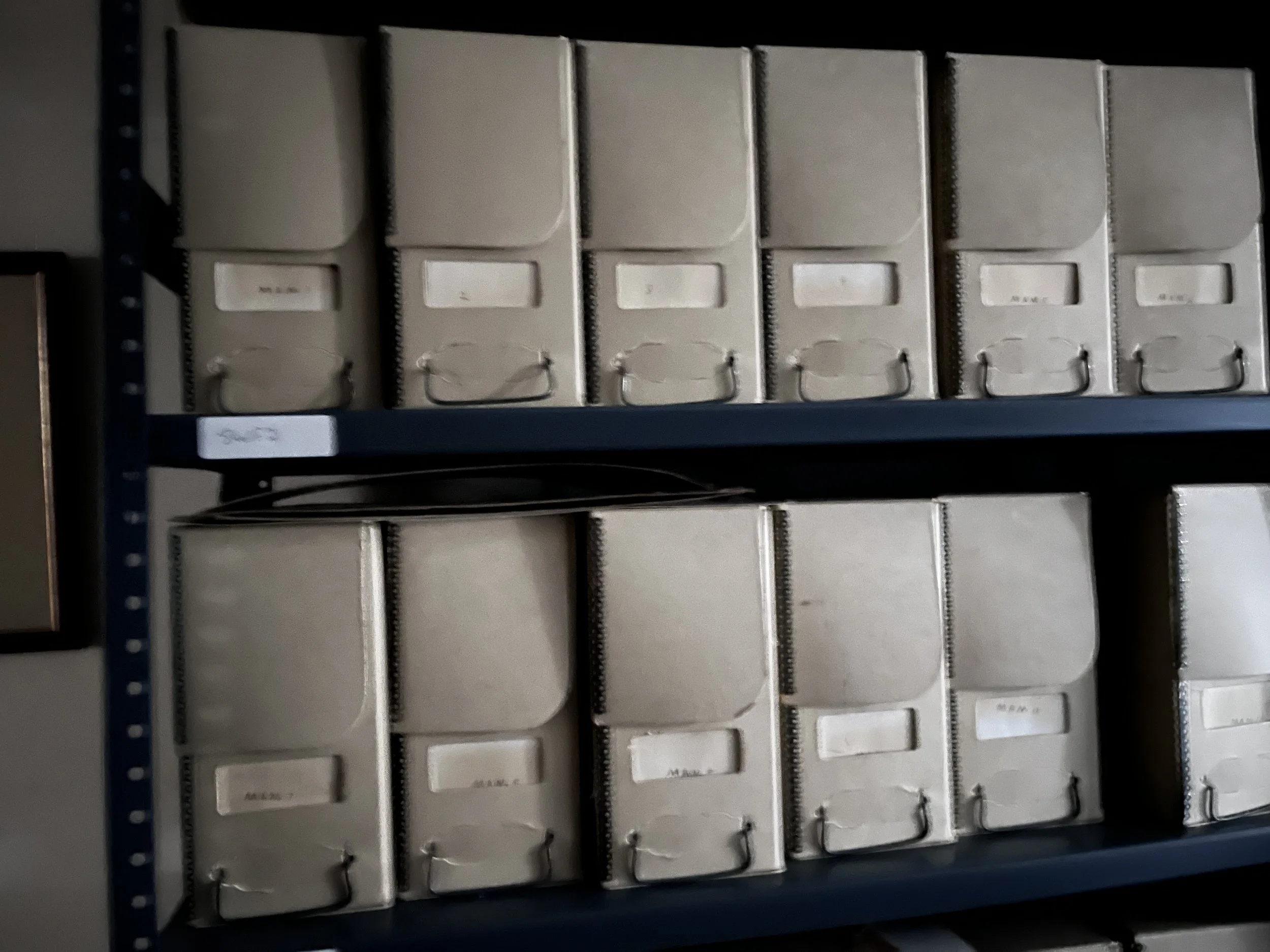 Shelf filled with beige binders labeled with handwritten or printed labels.