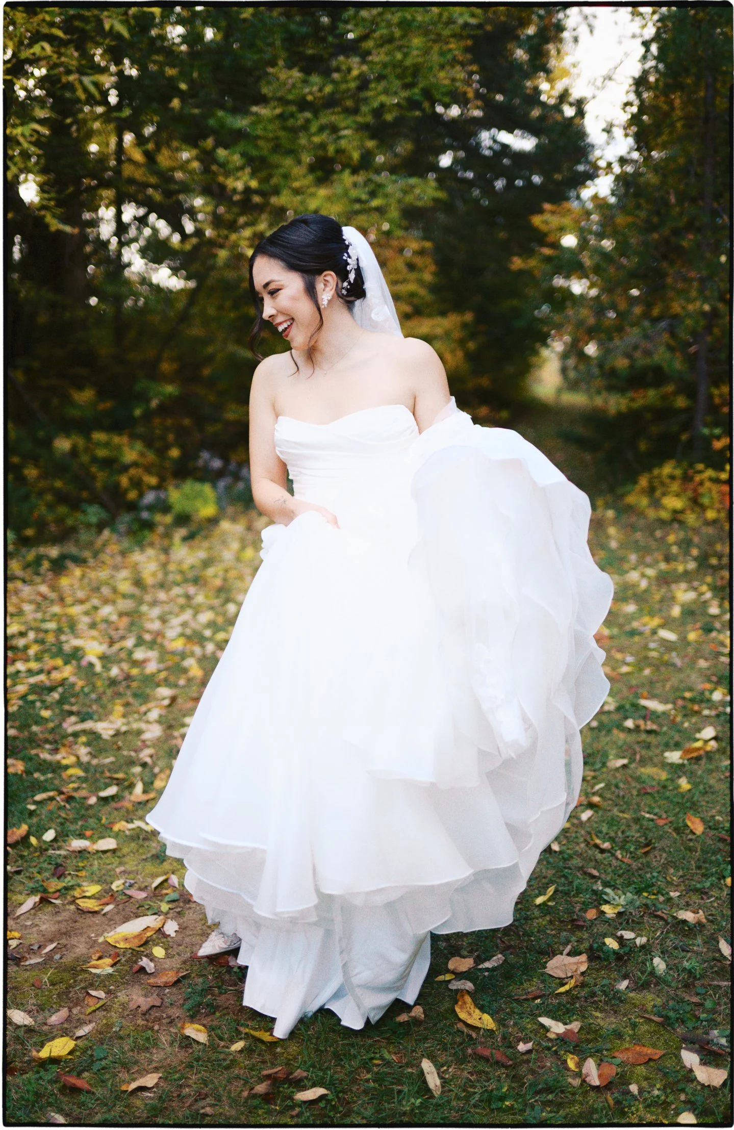 A bride in a white wedding dress holding her skirt outdoors in a park with fall foliage.Ottawa Wedding Photo, film wedding, Kodak wedding, 35mm wedding