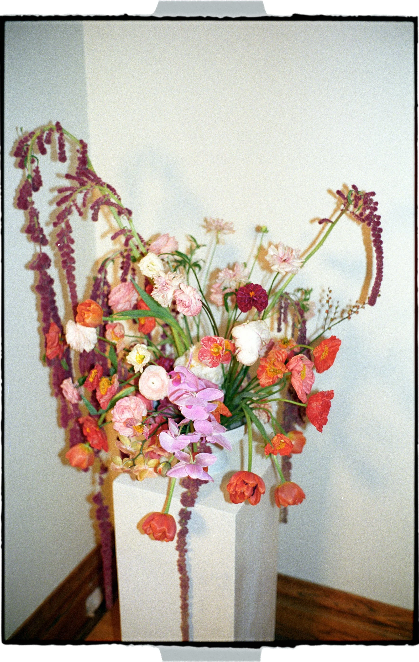 Colorful flower arrangement with pink, white, orange, and purple flowers in a white vase.