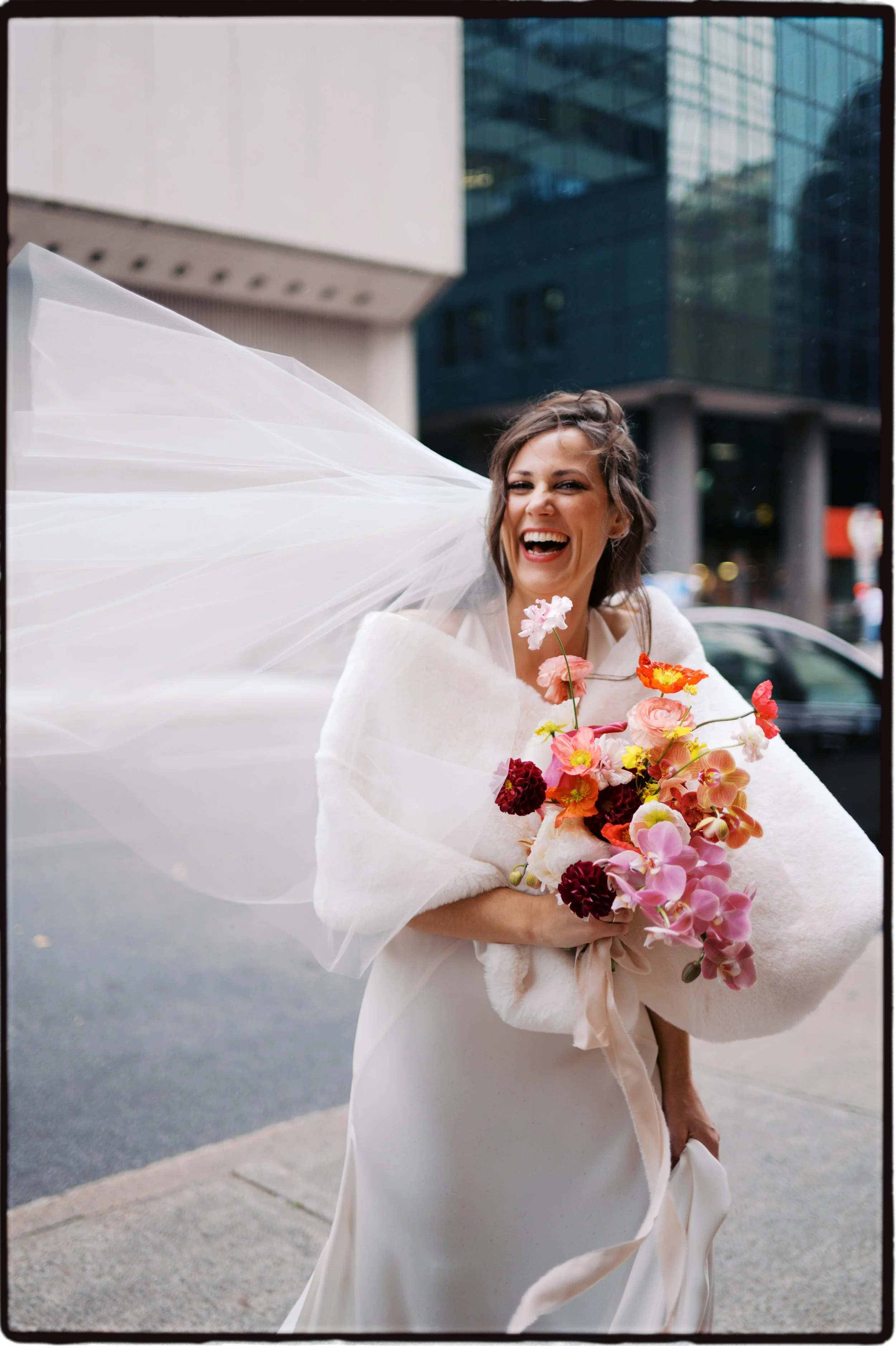 A woman in wedding attire holding a bouquet of pink and red flowers, smiling and twirling outdoors in an urban setting.Ottawa Wedding Photo, film wedding, Kodak wedding, 35mm wedding