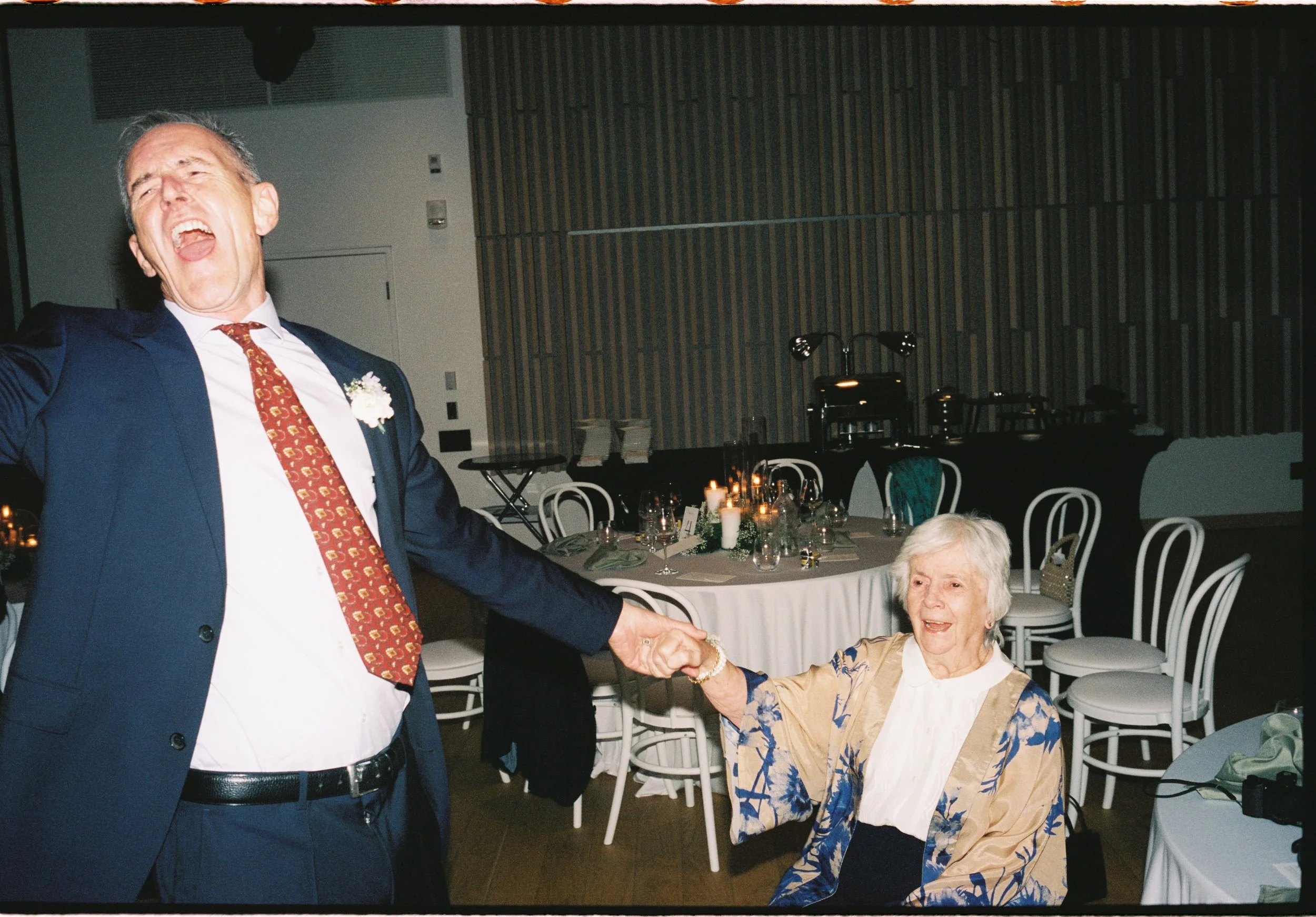 A man in a suit and a woman in a dress holding hands at a celebration or wedding reception