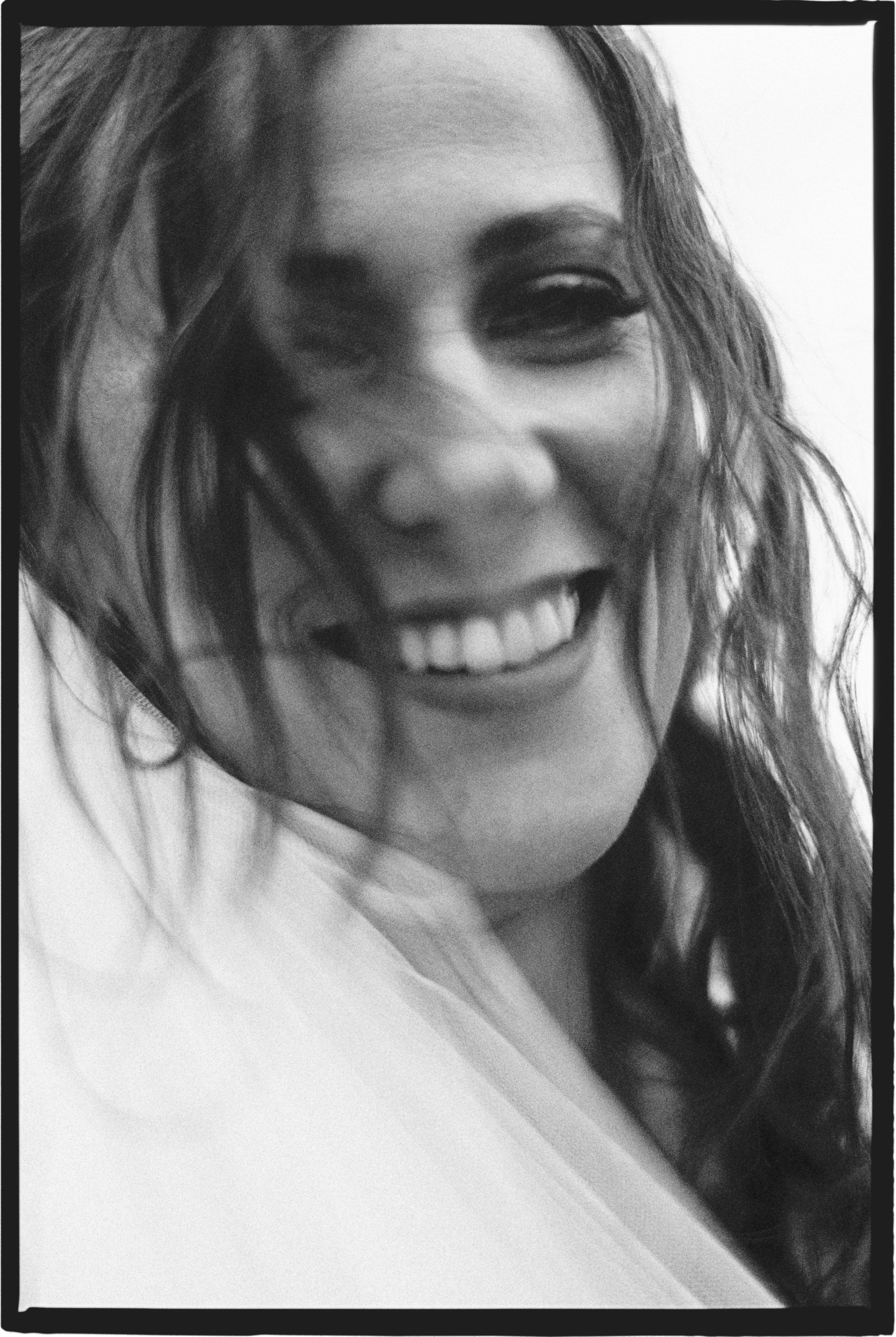 Close-up black and white photo of a woman smiling with hair blowing across her face.