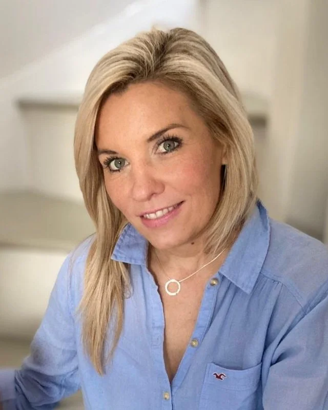 A photo of Kirsten Dunlop smiling and wearing a blue dress shirt with a silver necklace.