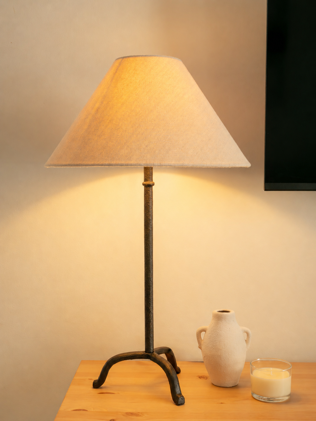 A table lamp with a fabric lampshade, a ceramic vase, and a lit candle on a wooden table.