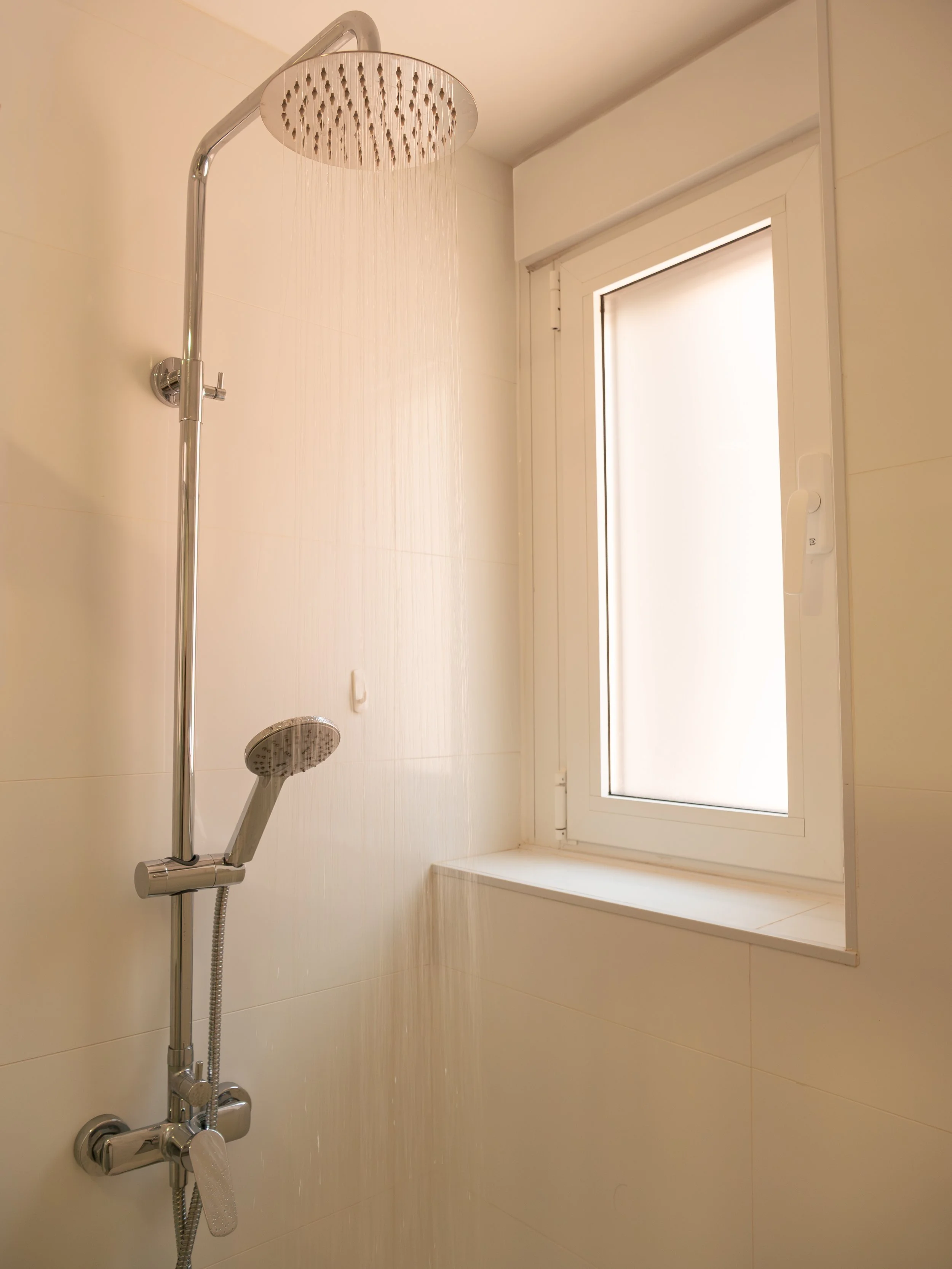 Shower with a rain shower head and handheld spray, white walls, a large window with frosted glass.