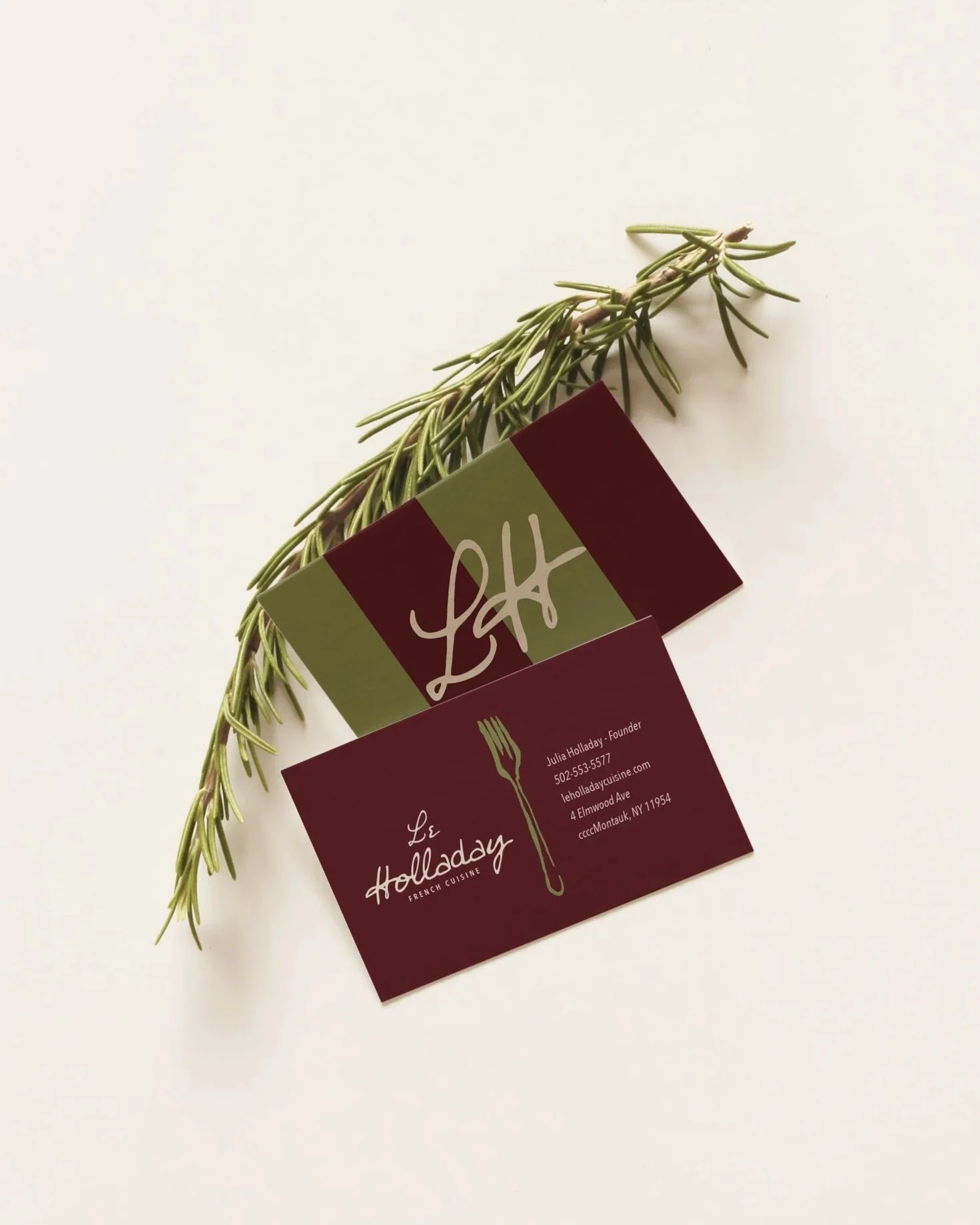 Business card for Le Holladay, a French cuisine restaurant, placed on a white surface with a sprig of rosemary.