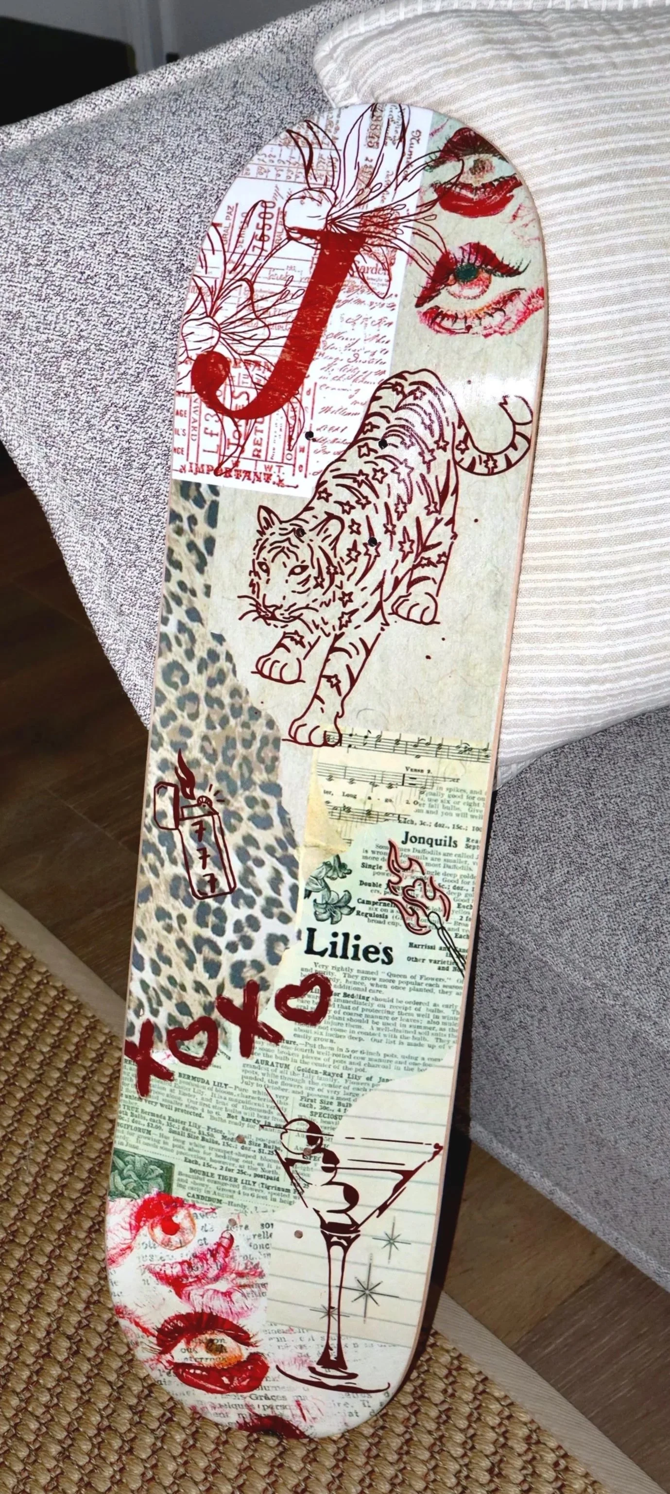 Decorative skateboard deck with collage-style artwork including a tiger, lips, eyes, cocktail glass, flowers, and text, with a red and white color theme.