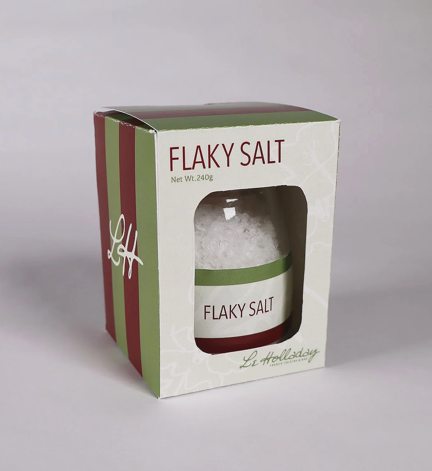 Box of flaky salt with a clear window showing the salt crystals inside, labeled 'Flaky Salt' and wrapped in green and red packaging with a white background.