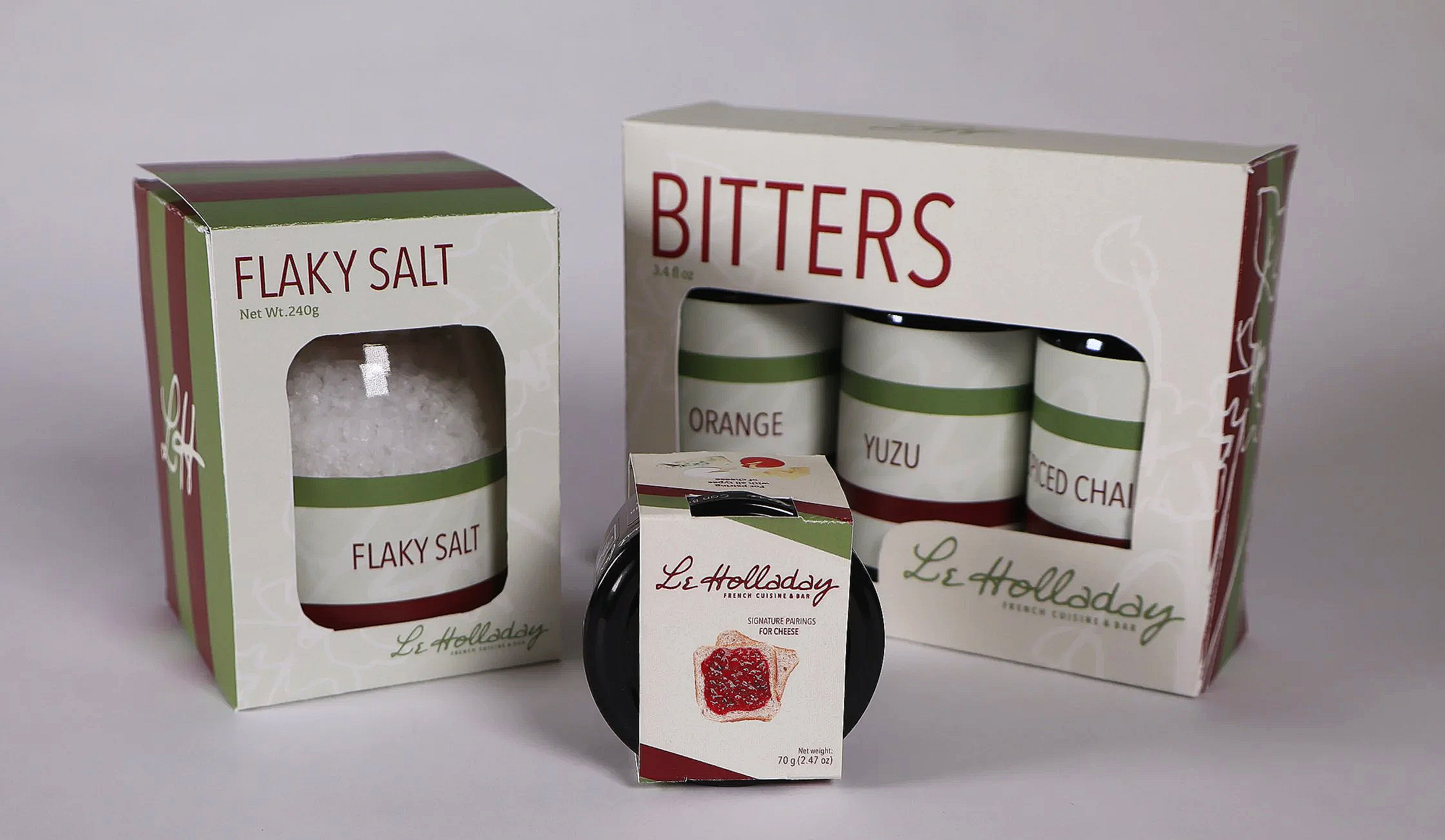 Boxes of flavored salts, including flaky salt, and a set of three small jars labeled orange, yuzu, and smoked chard, with a small container of cheese accompaniment.