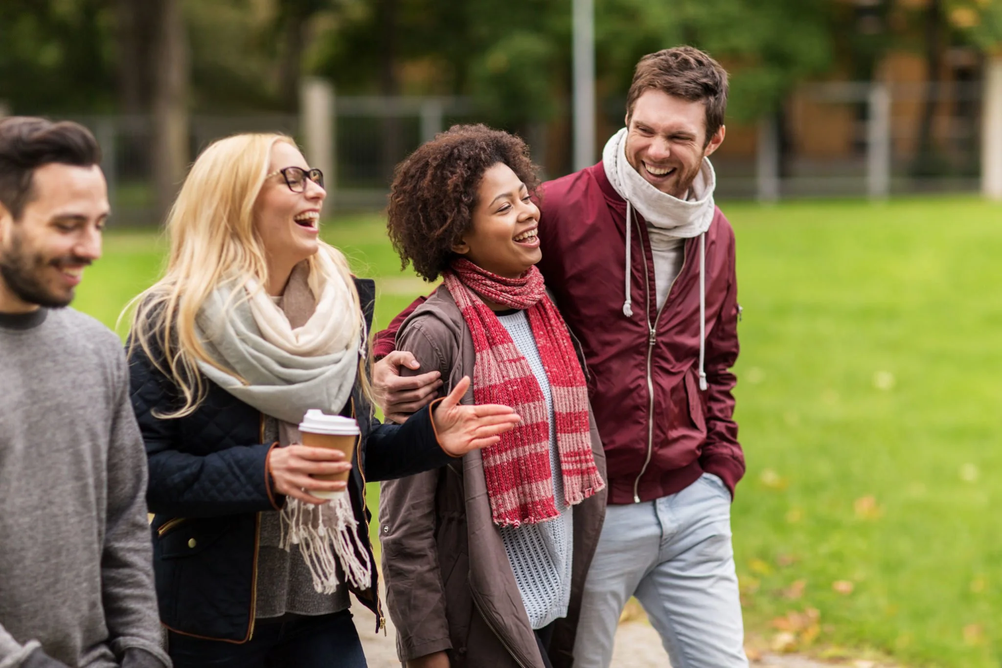 A group of five young adults walking together outdoors in a park, smiling and engaging in conversation.