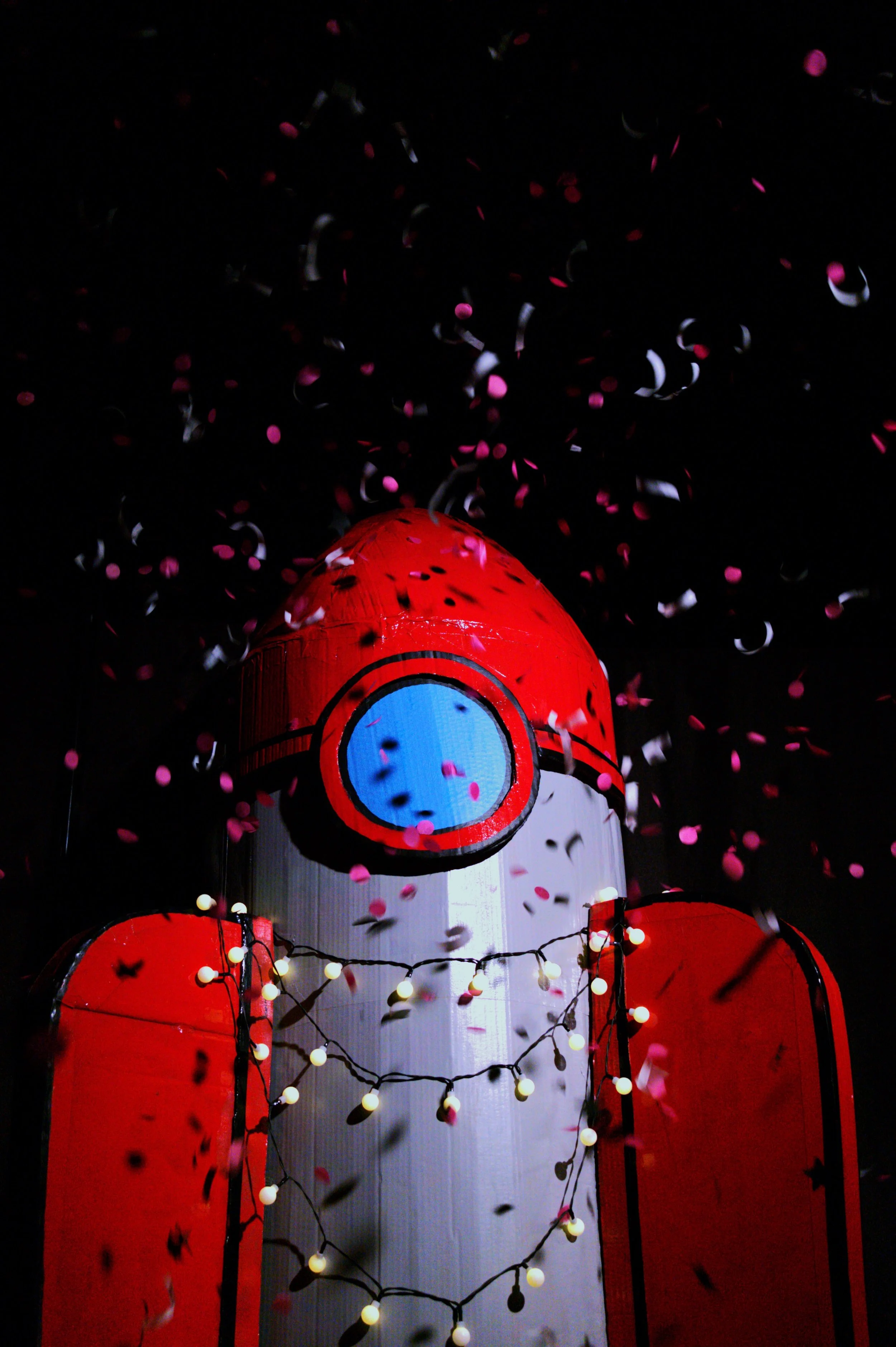 Décoration de lancement de fusée en forme de rocket en papier avec des lumières et des confettis rose, noir, blanc, fond noir.
