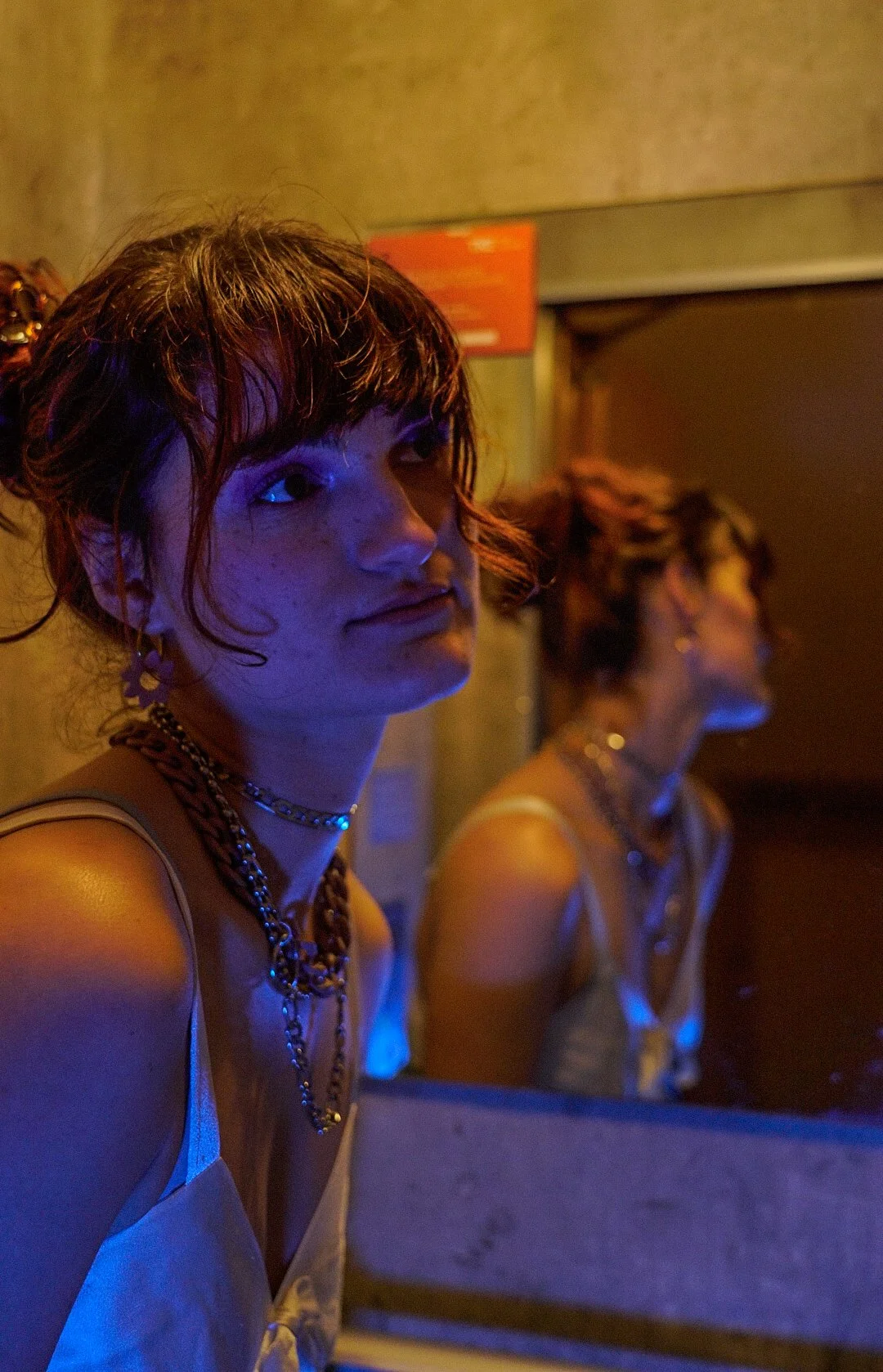 Deux jeunes femmes avec des cheveux bouclés ou ondulés portent des bijoux et sont dans un environnement avec une lumière bleue ou violette, probablement lors d'une soirée ou d'un événement.