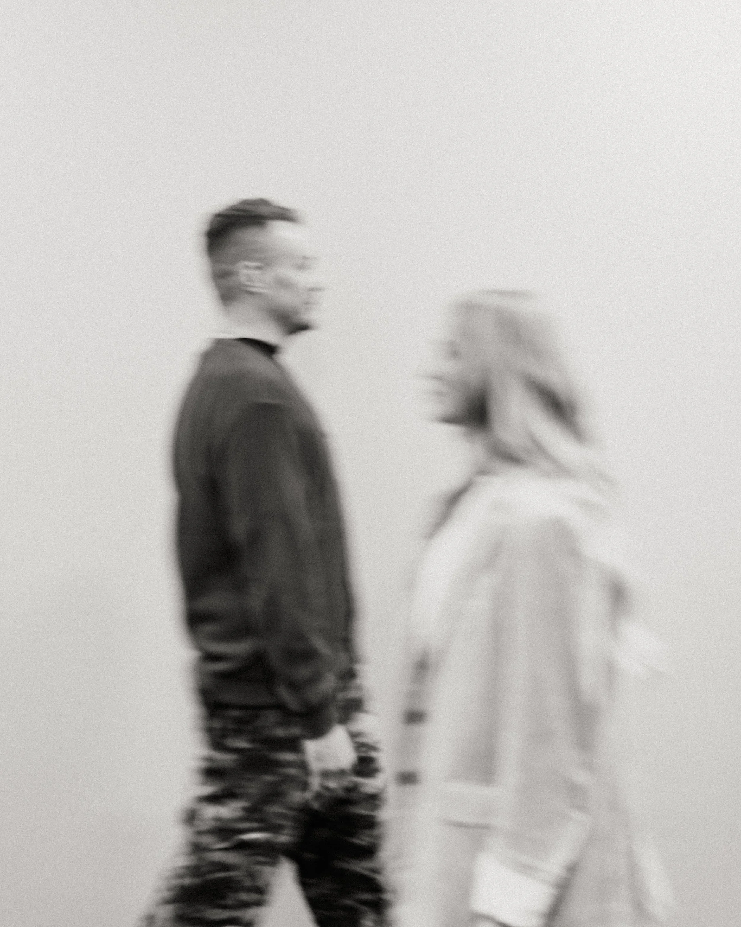 Blurry black-and-white photo of a man and woman standing and facing each other against a plain background walking into confidence.