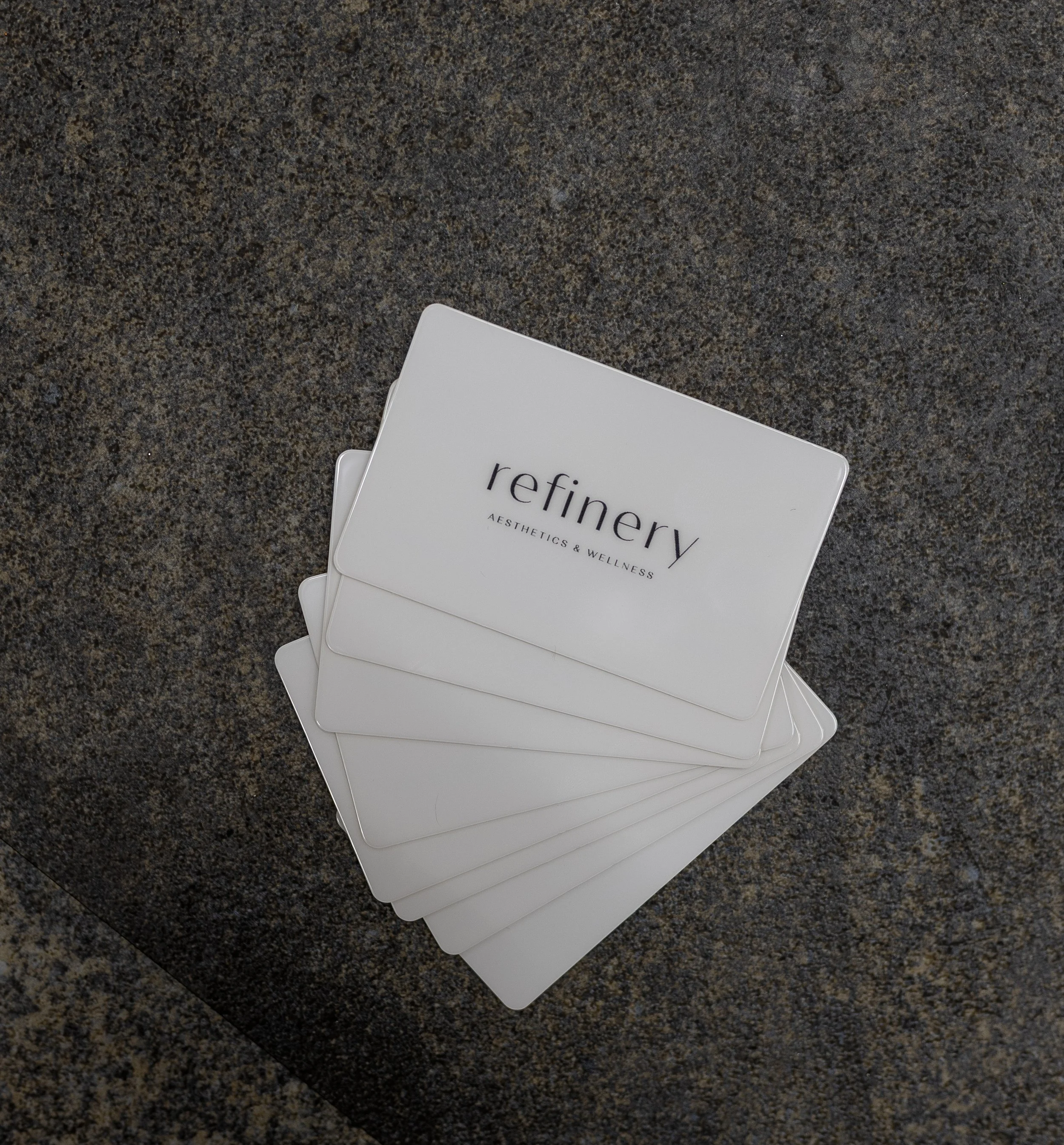 A small white card with the word "refinery" on it, partially visible, placed on a dark, speckled countertop.