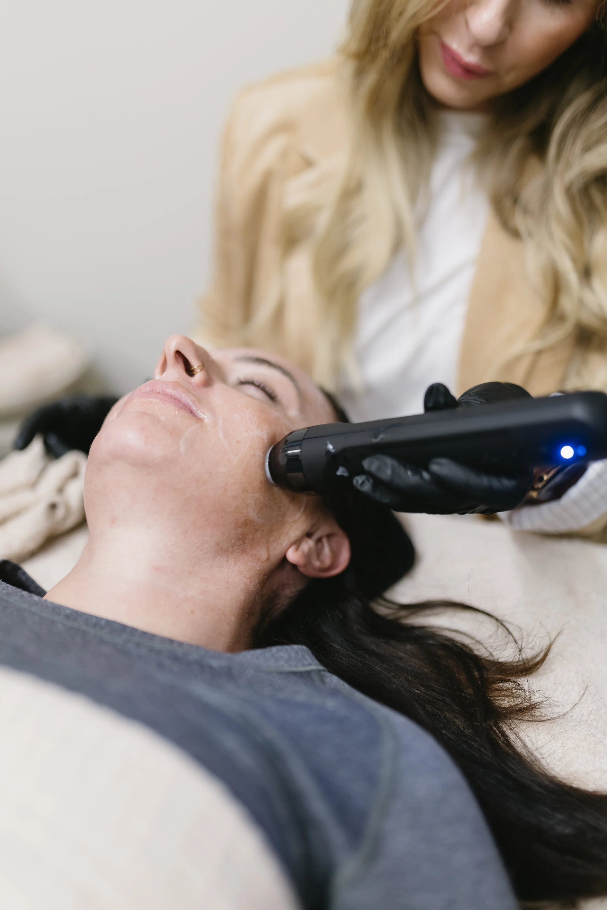 A woman getting a facial treatment with Glo2 facial with radiofrequency on her face at a skincare clinic, Refinery Aesthetics & Wellness.