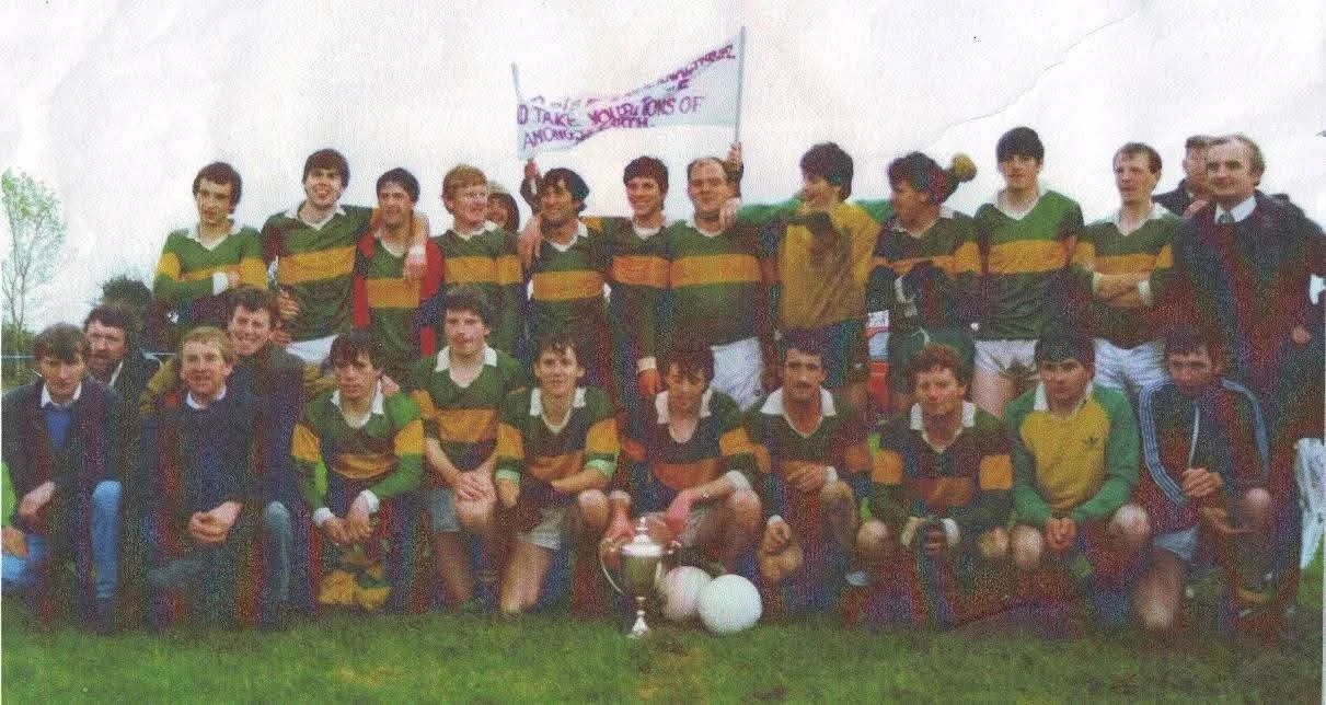 Group of young boys in green and yellow sports uniforms posing outdoors with trophies and balloons.