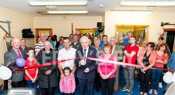Group of people participating in a ribbon-cutting ceremony, with a man in a suit holding scissors, in a decorated room.