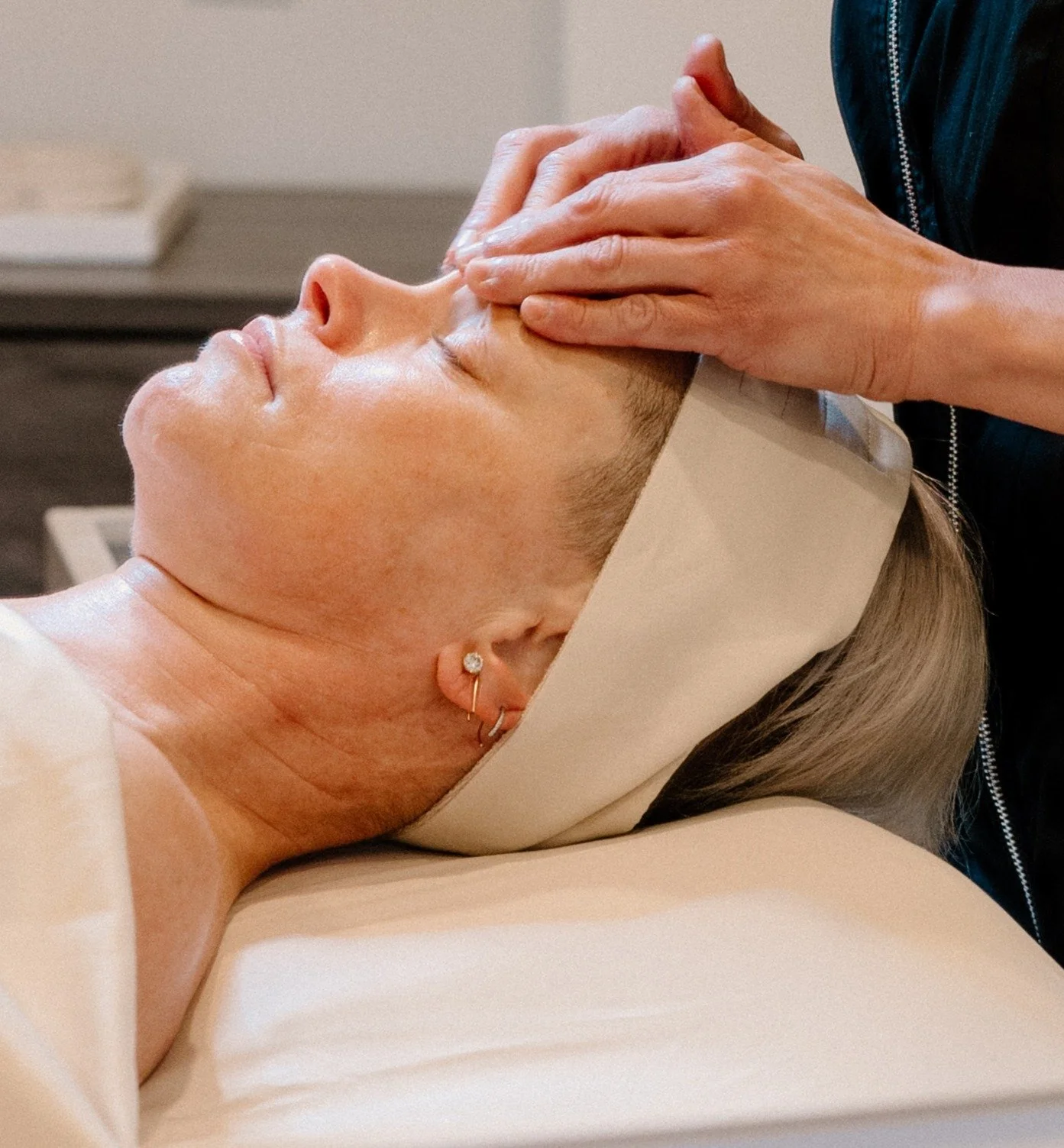 A woman receiving a facial treatment while lying on a treatment bed with her eyes closed.