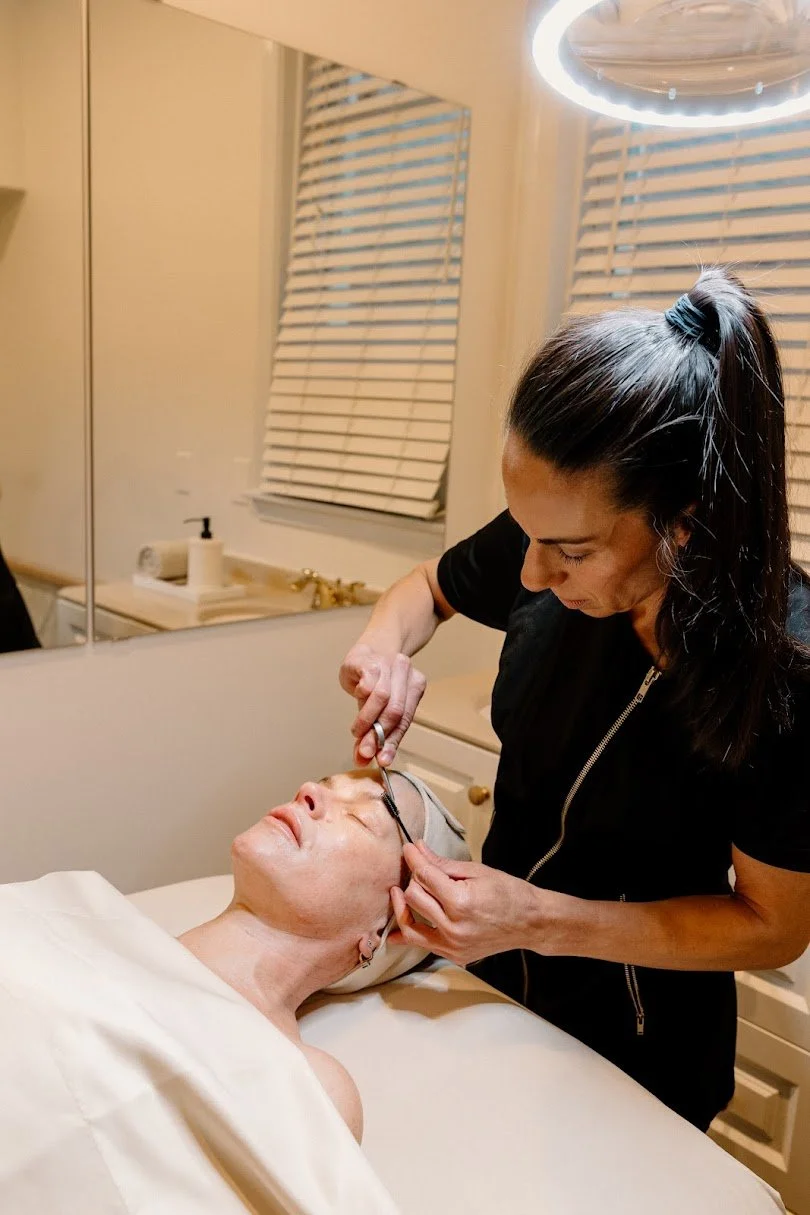 A woman receiving an eyelash extension treatment from a Liz Clapsis.