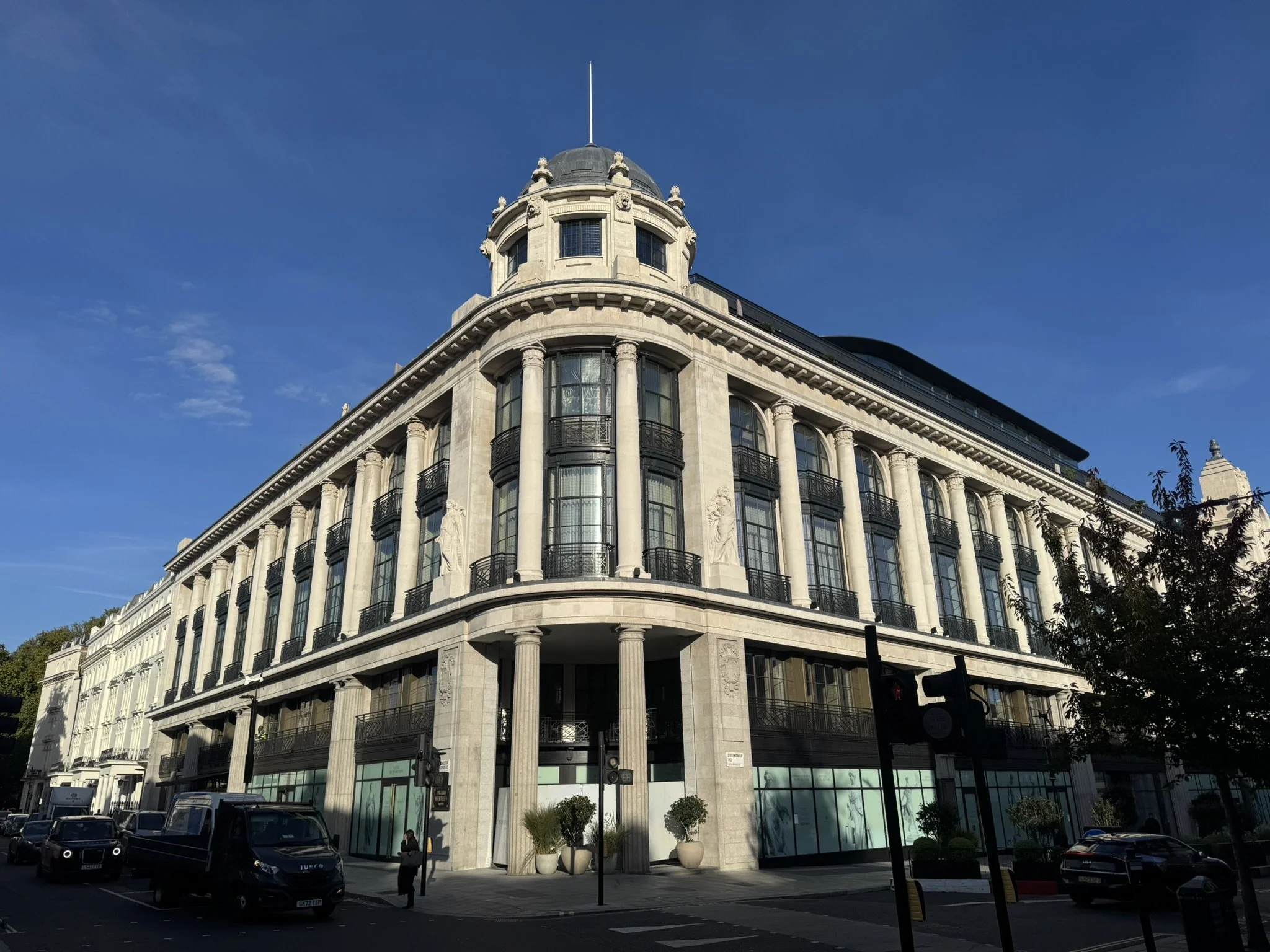 A large white historic building with columns and large windows on a city street during daytime.