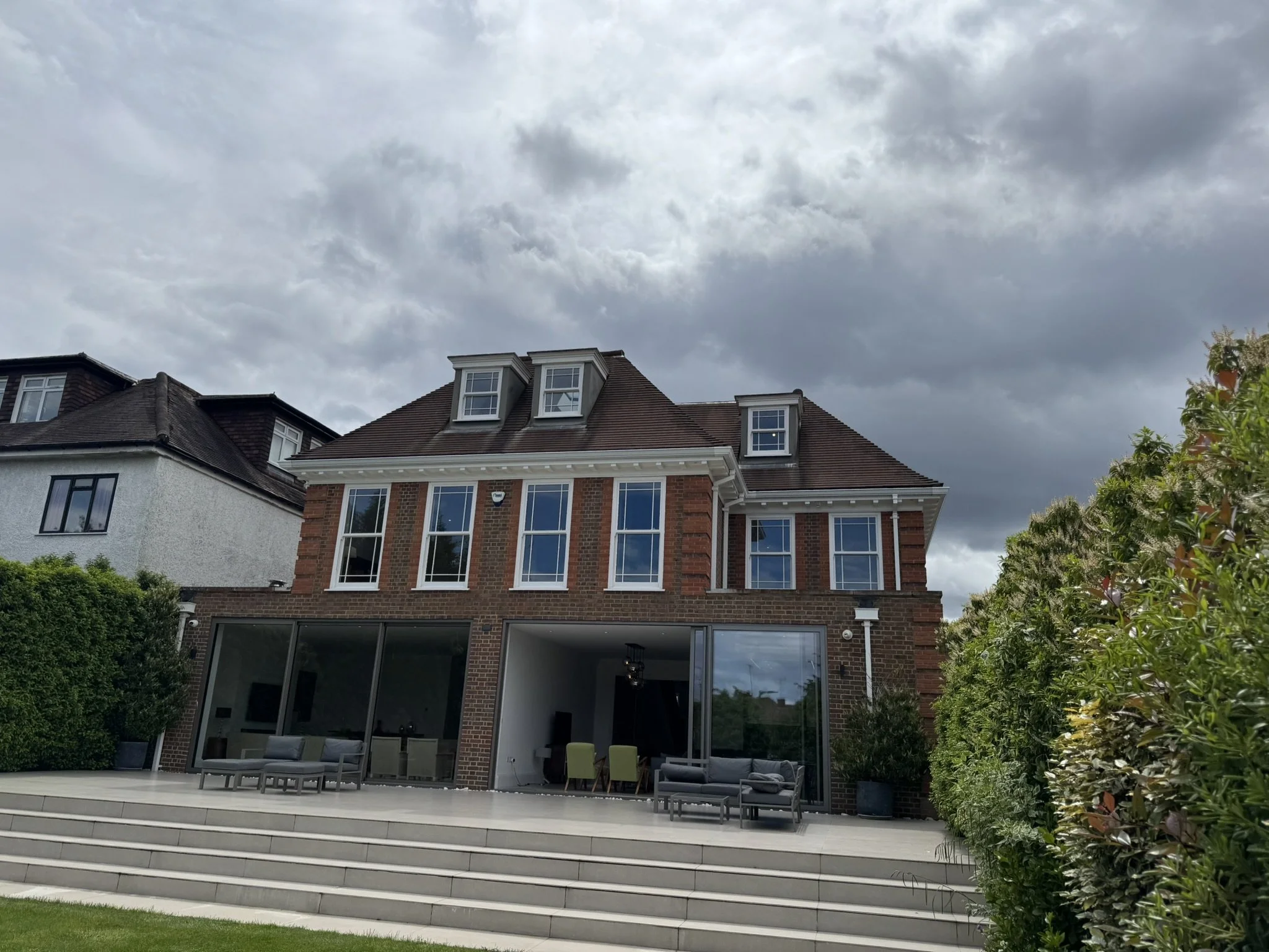 Rear view of a brick house with large glass doors and multiple windows under a cloudy sky.