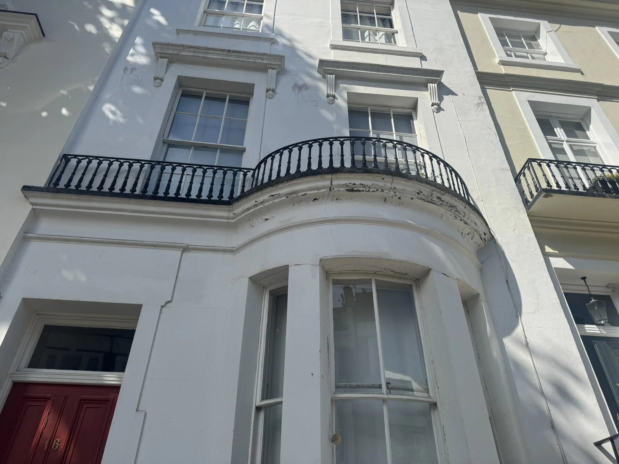 A close-up view of a white building with multiple windows and balconies, featuring decorative architectural details and black wrought iron railings.
