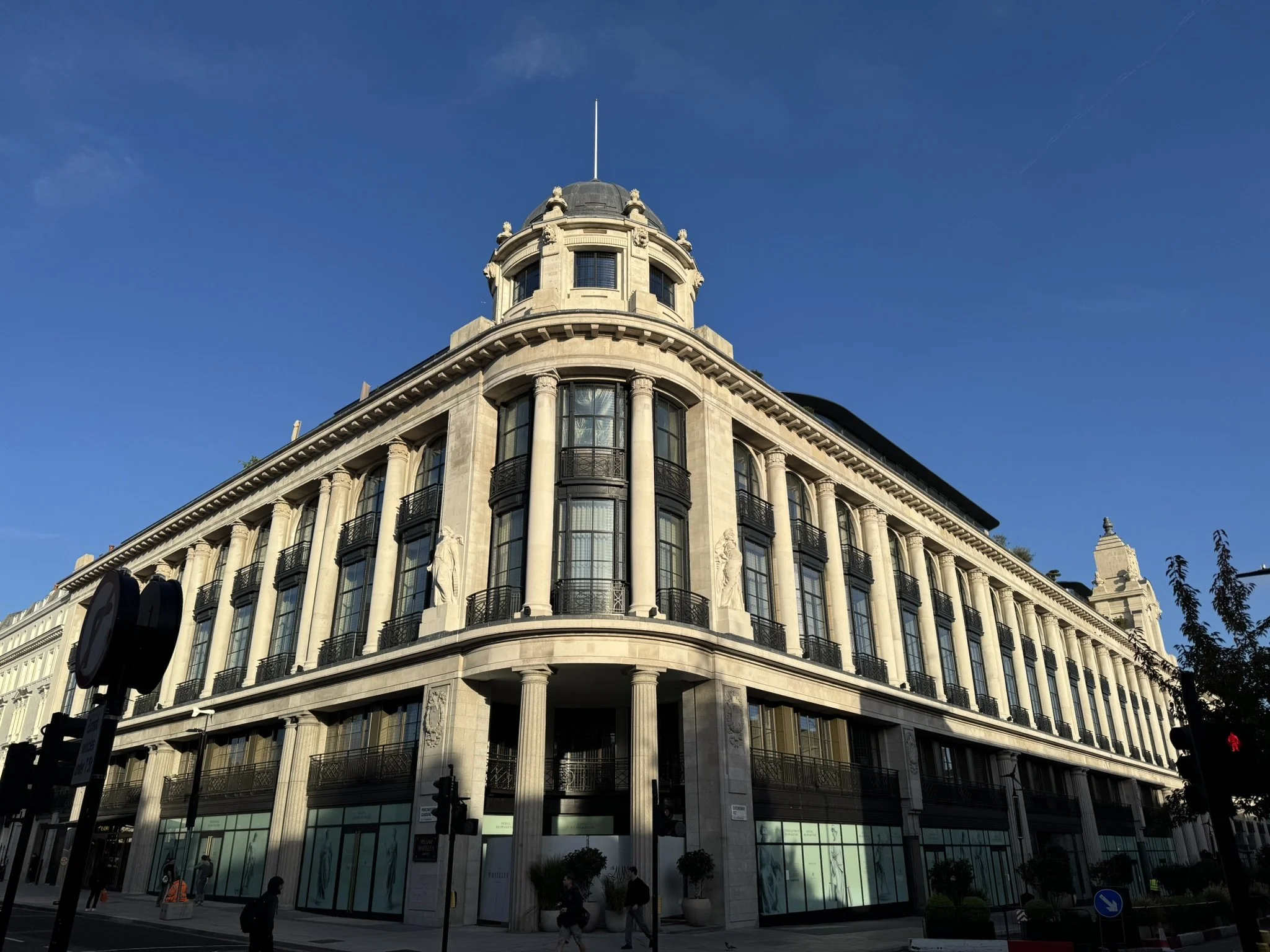 A historic multi-story building with neoclassical architecture, featuring columns, sculptures, and large windows, under a clear blue sky.