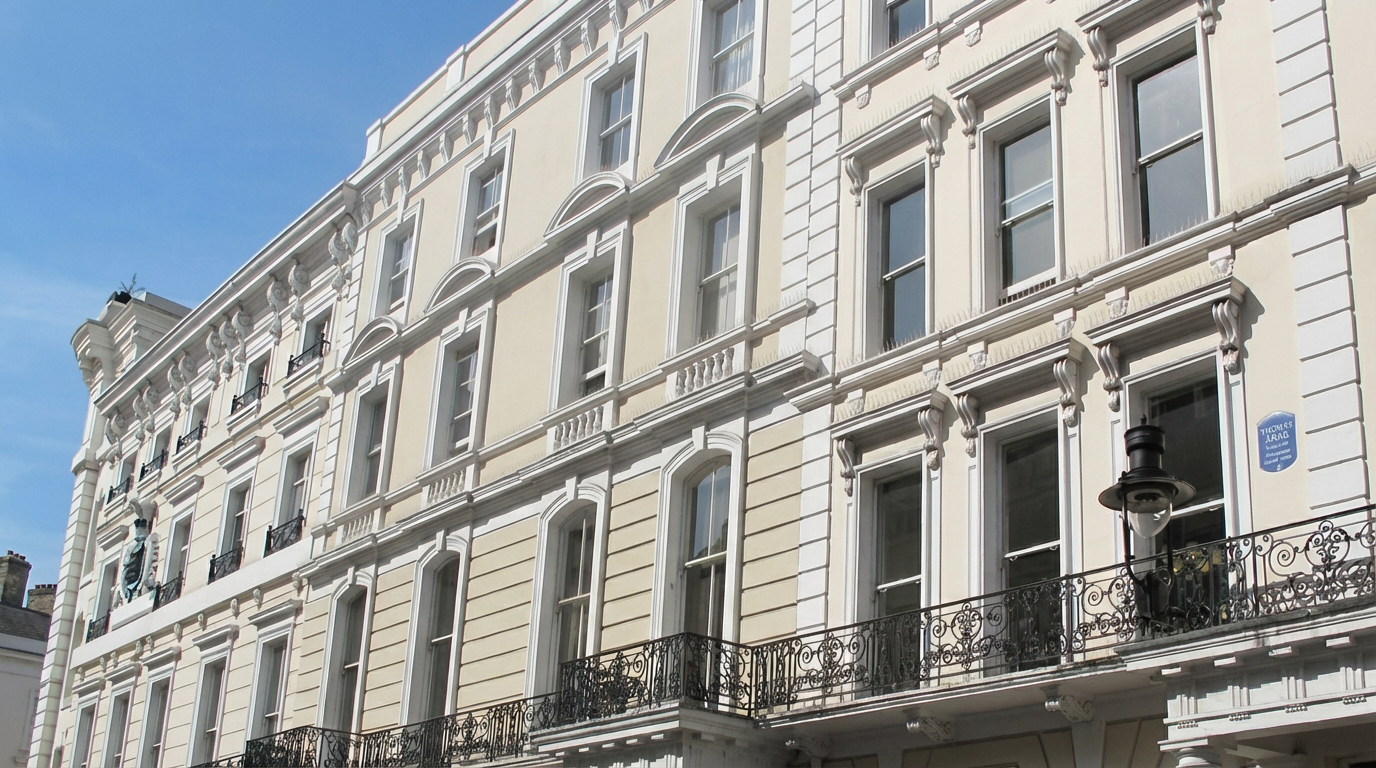 A beige-colored multi-story building with decorative architectural details and wrought iron balconies under a blue sky.