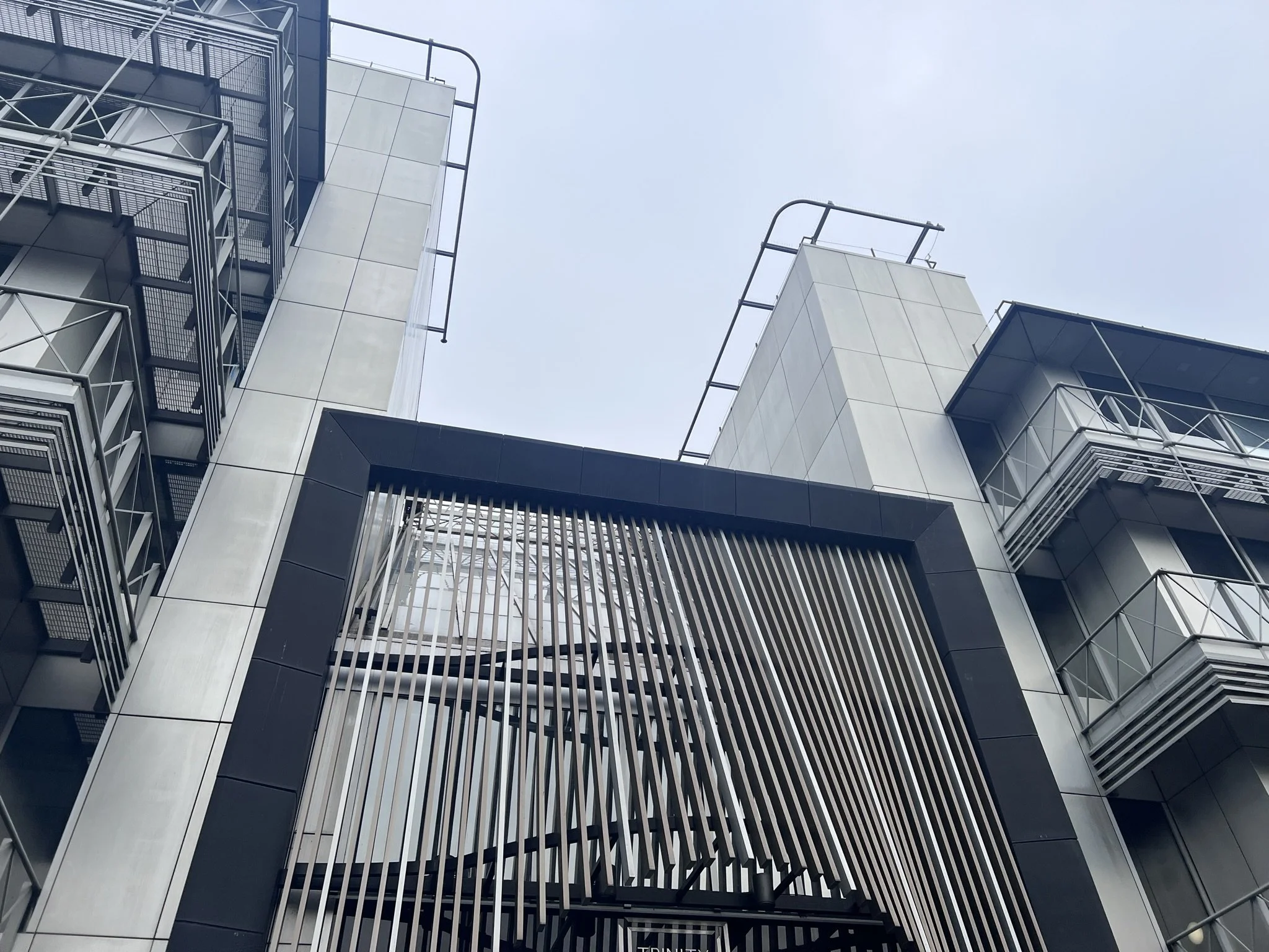 Low-angle view of a modern building with balconies, metal railings, and a central structure with vertical slats, against a clear sky.