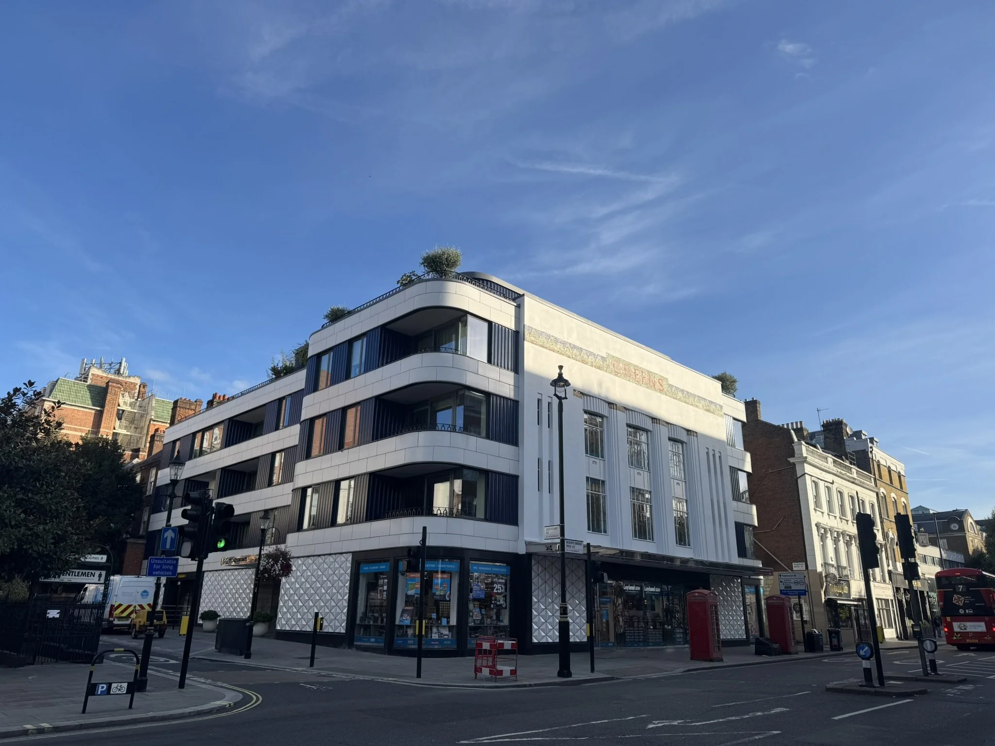 A modern multi-story building with white exterior panels and large glass windows, situated on a city street corner, with a clear blue sky overhead.