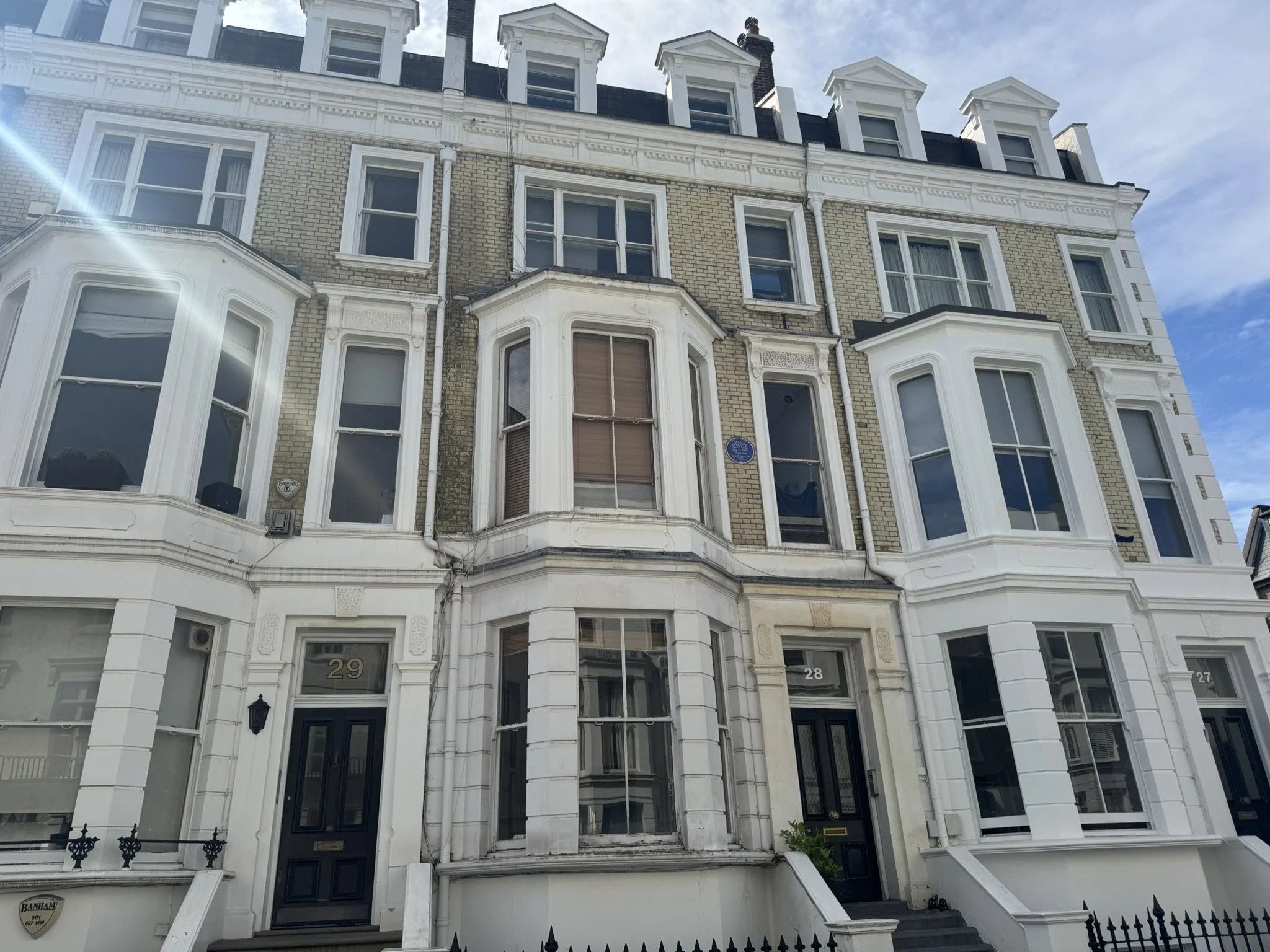 Four-story Victorian-style brick apartment building with bay windows and front doors numbered 29 and 28, set against a partly cloudy sky.