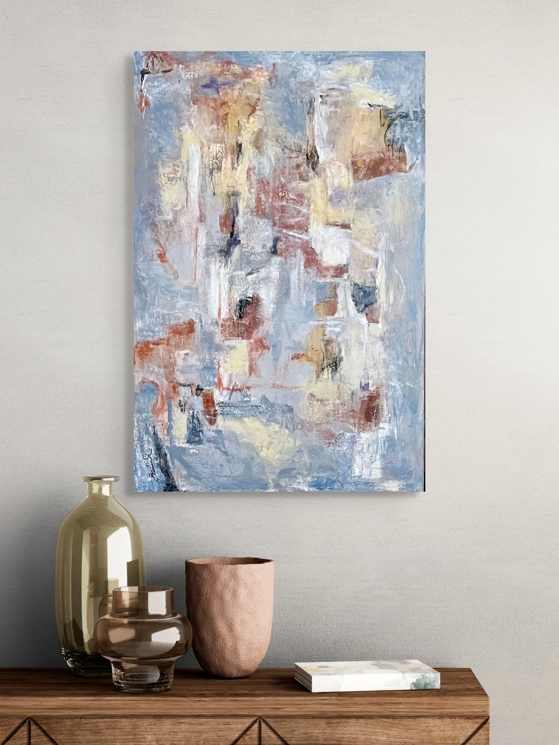 A close-up of a wall-mounted abstract painting with soft pastel colors above a wooden sideboard decorated with vases and a marble coaster.