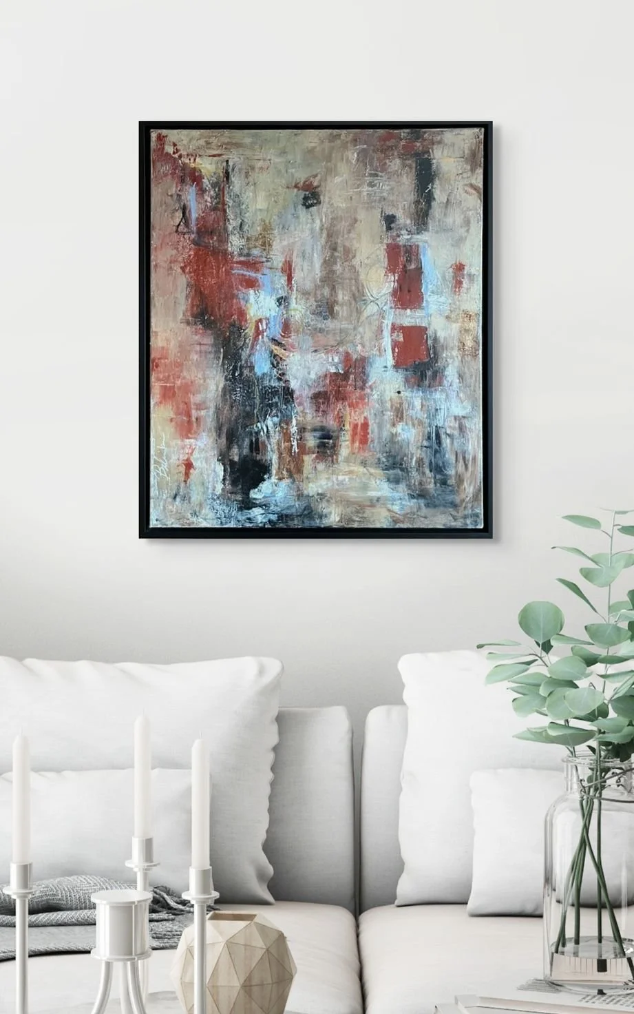 Abstract painting with red, black, beige, and blue colors hanging above a white sofa in a modern living room.