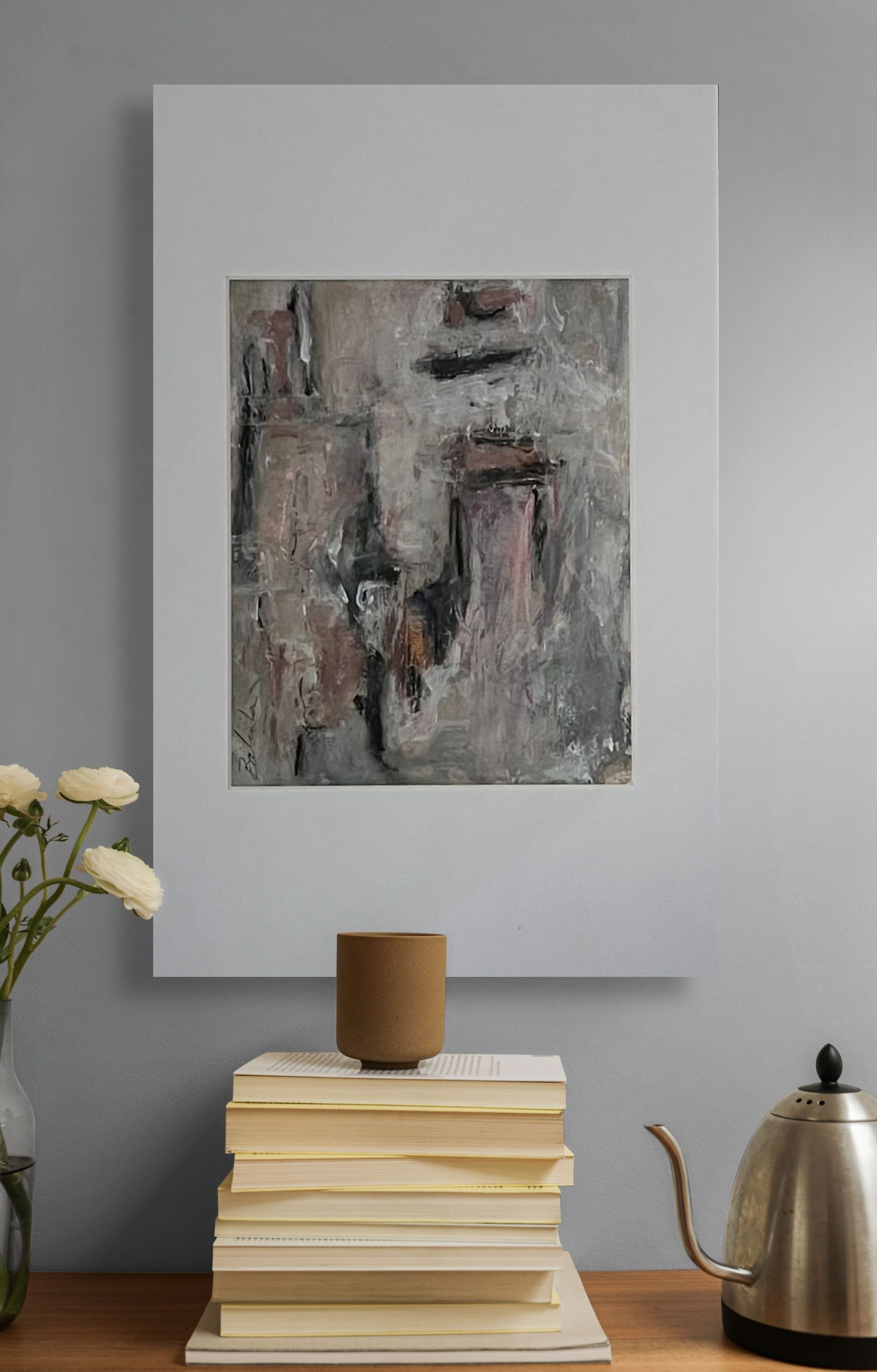 In a room with light gray walls, a framed abstract painting hangs above a stack of large beige books. On top of the books, there is a small matte brown pot. To the right, a metallic teapot with a curved spout and black handle is present. To the left, a vase with white flowers is partially visible.