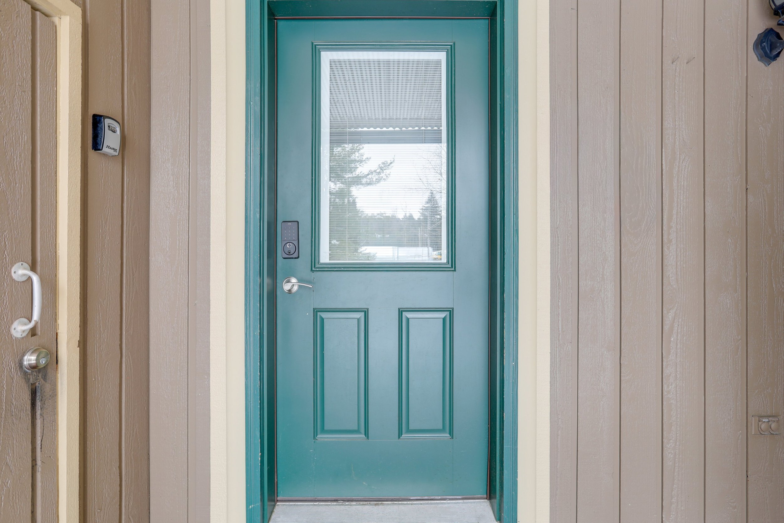 A front door with a large window, painted green, set in beige siding with vertical panels.