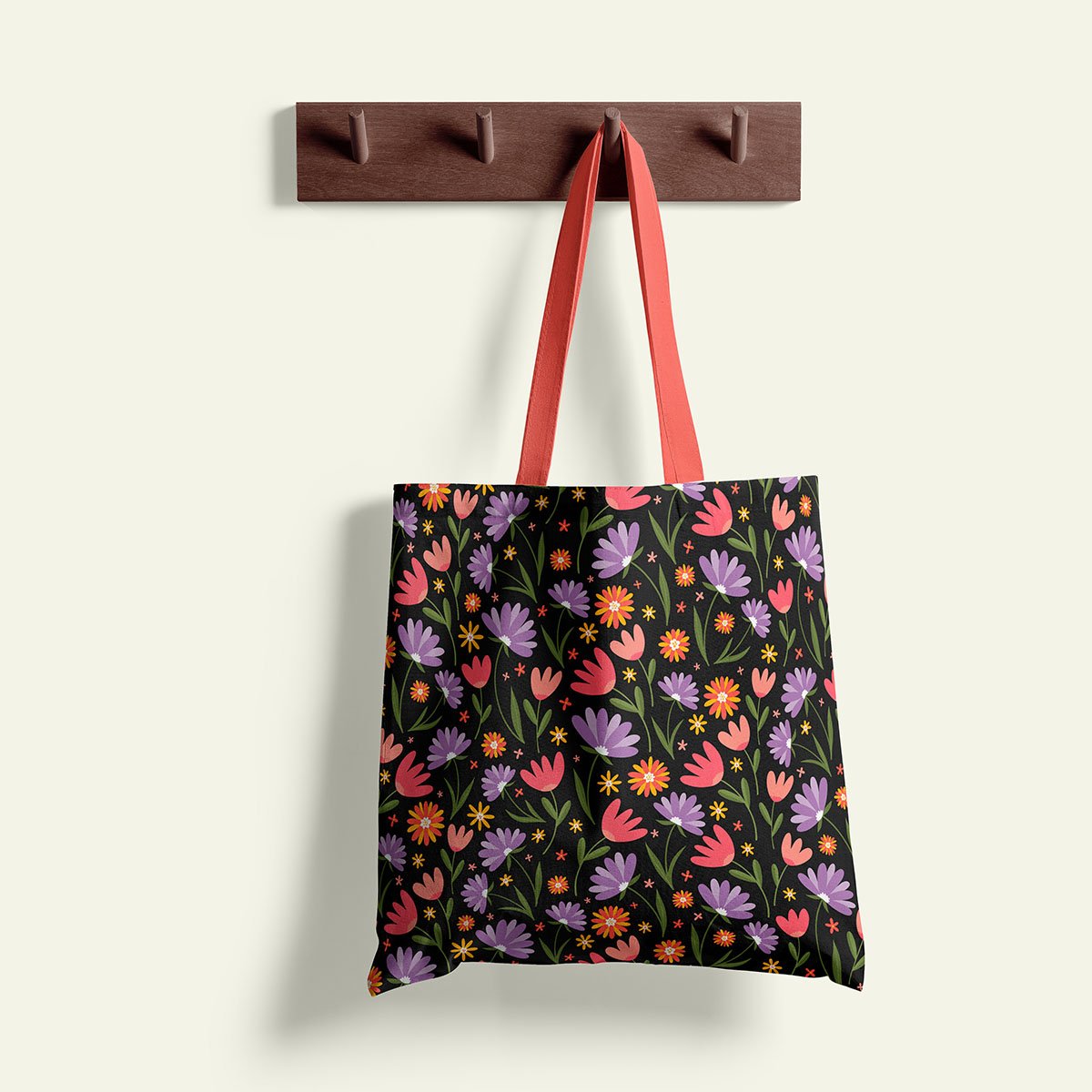A black tote bag with a colorful floral pattern hanging from a brown wall hook with red straps.