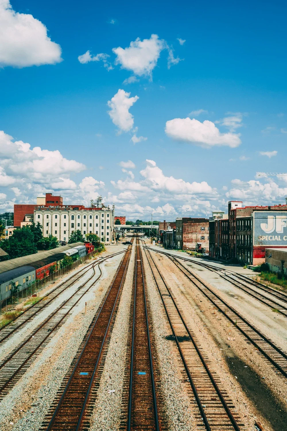 View of railway tracks extending into the distance in an urban area under a partly cloudy sky, with buildings on either side.